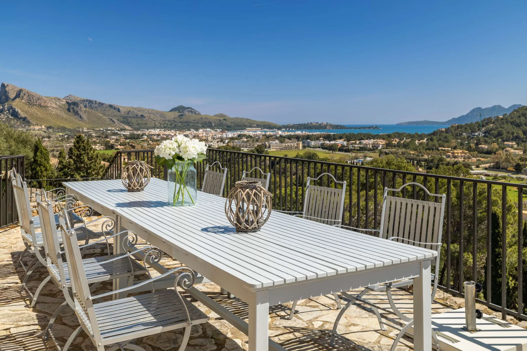 An outdoor dining area overlooks a coastal landscape from a terrace.