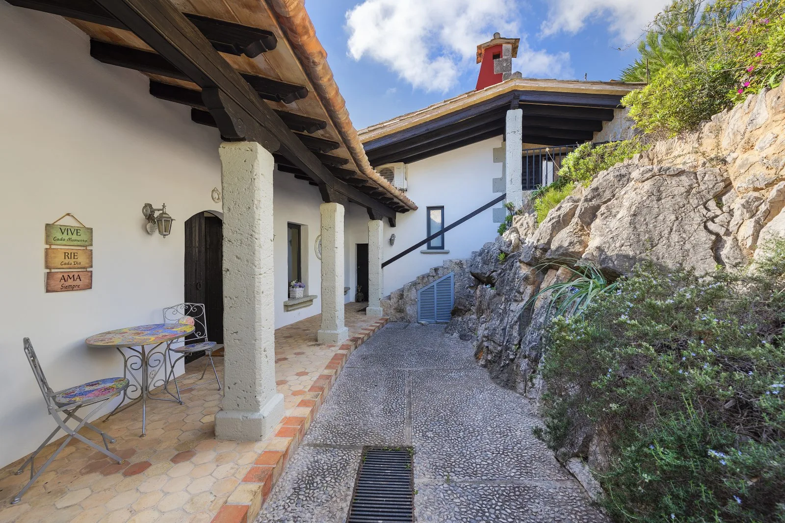A stone-paved passage runs beside a white building, with a rocky garden wall.