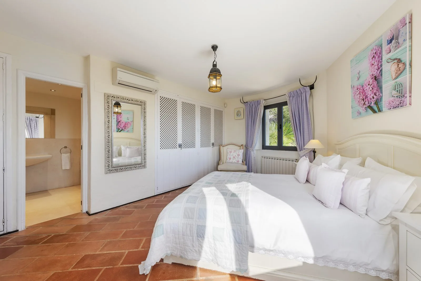 A bright bedroom with a large bed, patterned wall art, and a window.