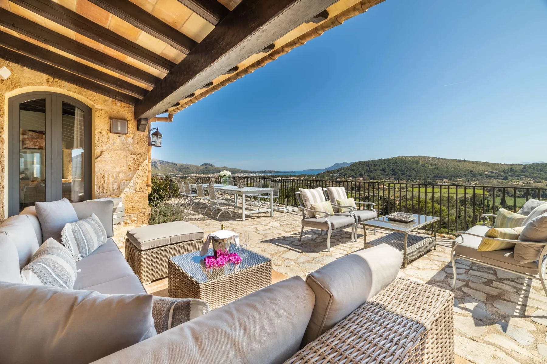 A sunny outdoor terrace has seating and a view of green hills.