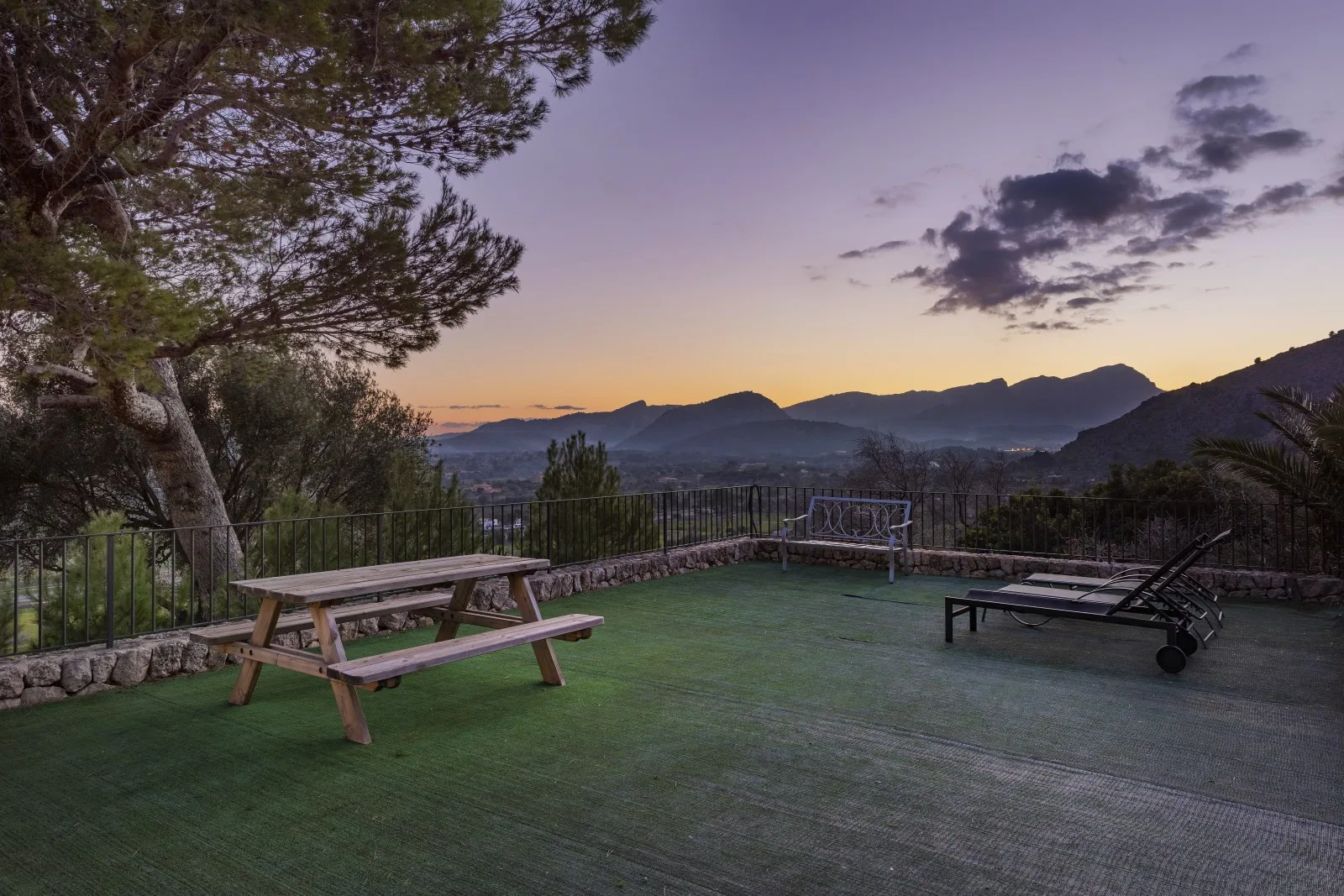 An outdoor terrace with picnic seating overlooks a mountain valley at dusk.