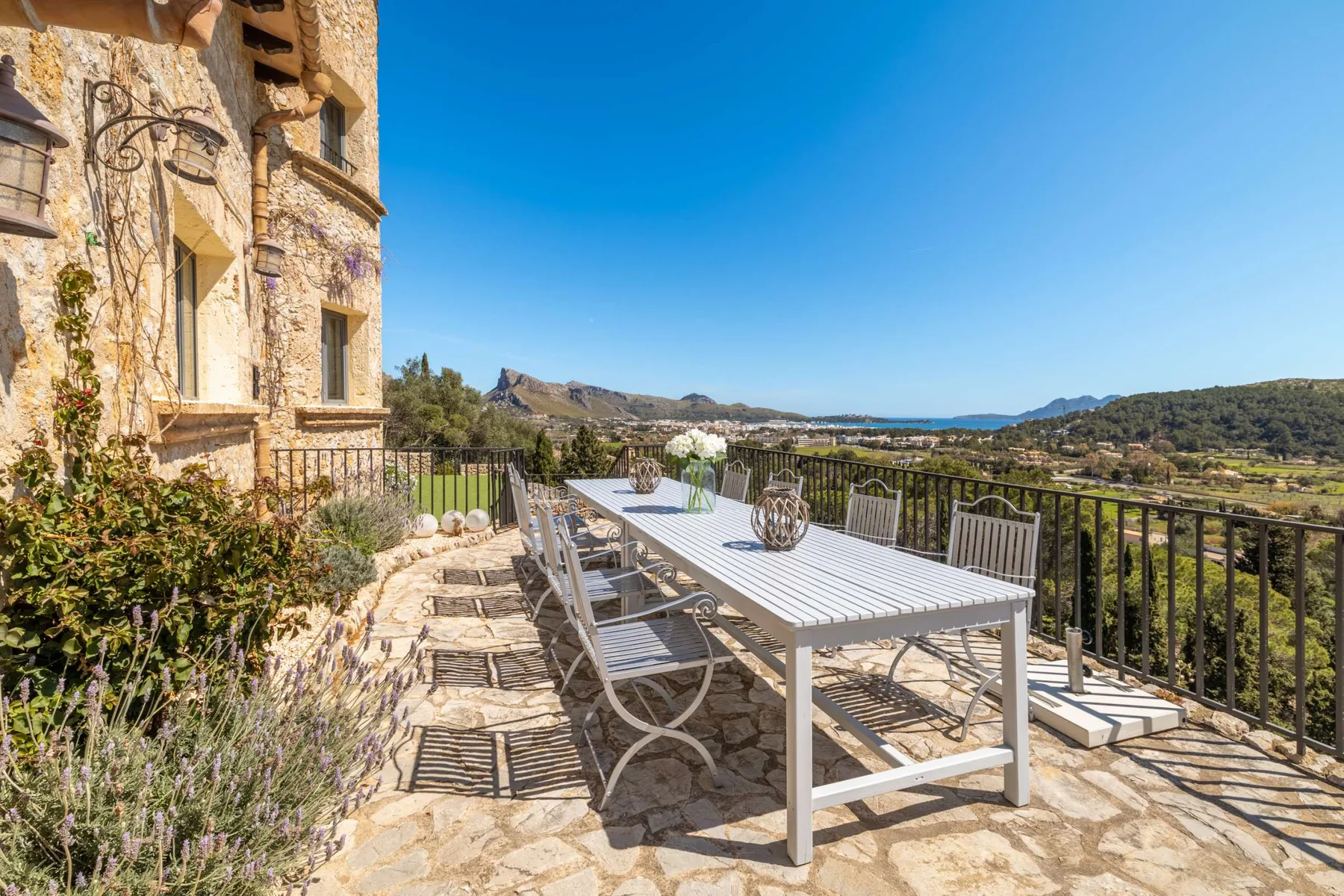 An outdoor dining area on a stone terrace overlooks a green valley.