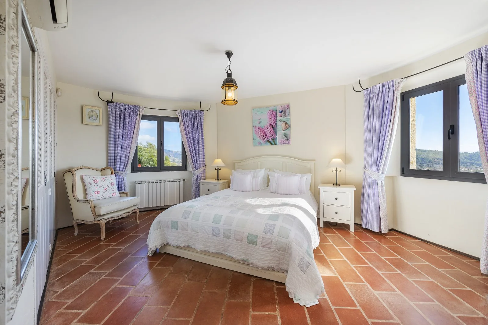 A bright bedroom with a double bed between two windows.