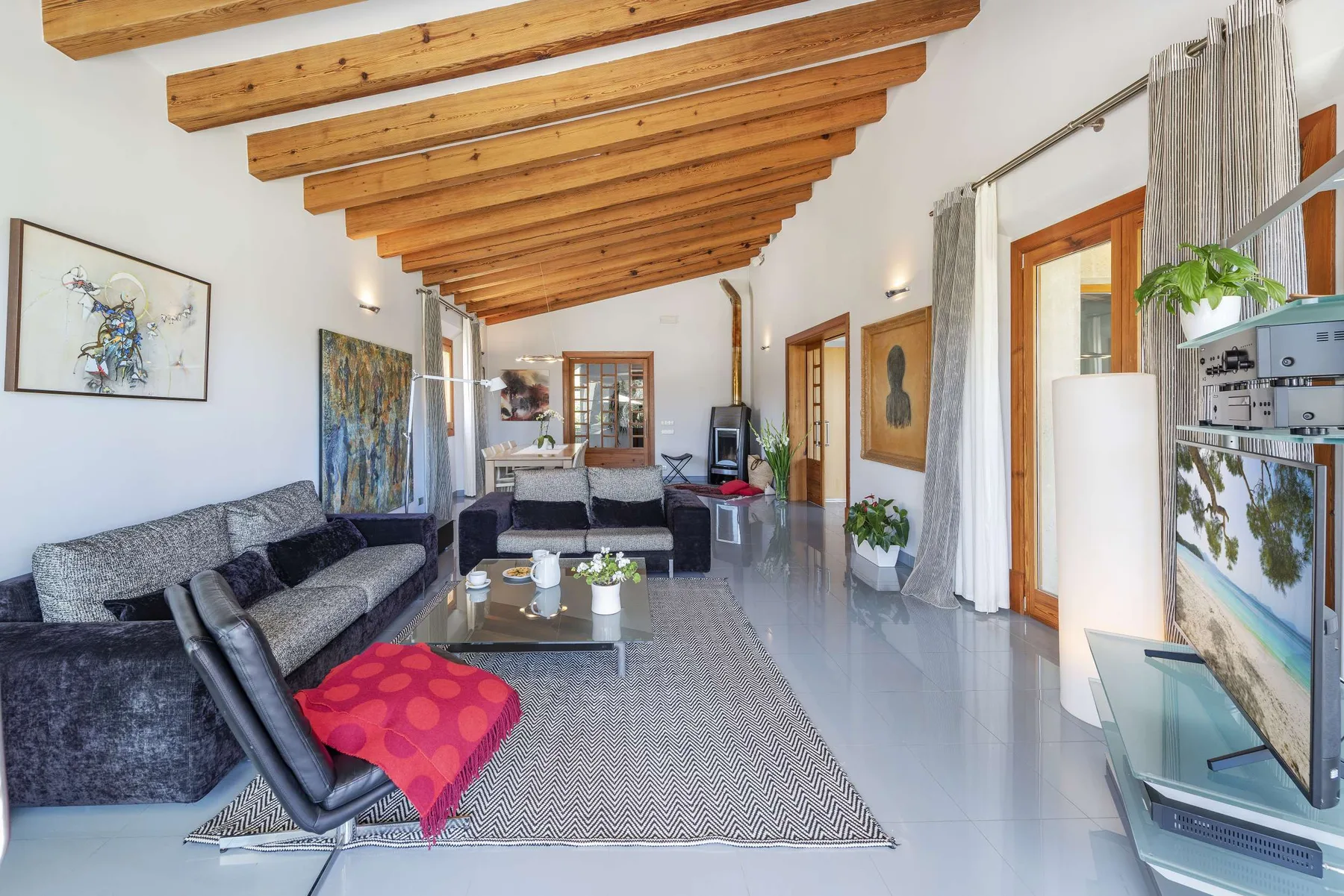A living room with seating around a low table beneath exposed wooden ceiling beams.
