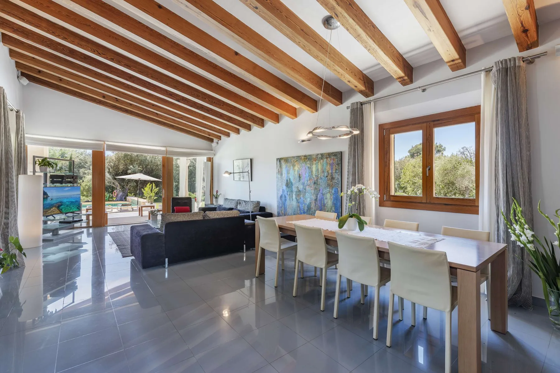 An open-plan living and dining room with exposed wooden ceiling beams.