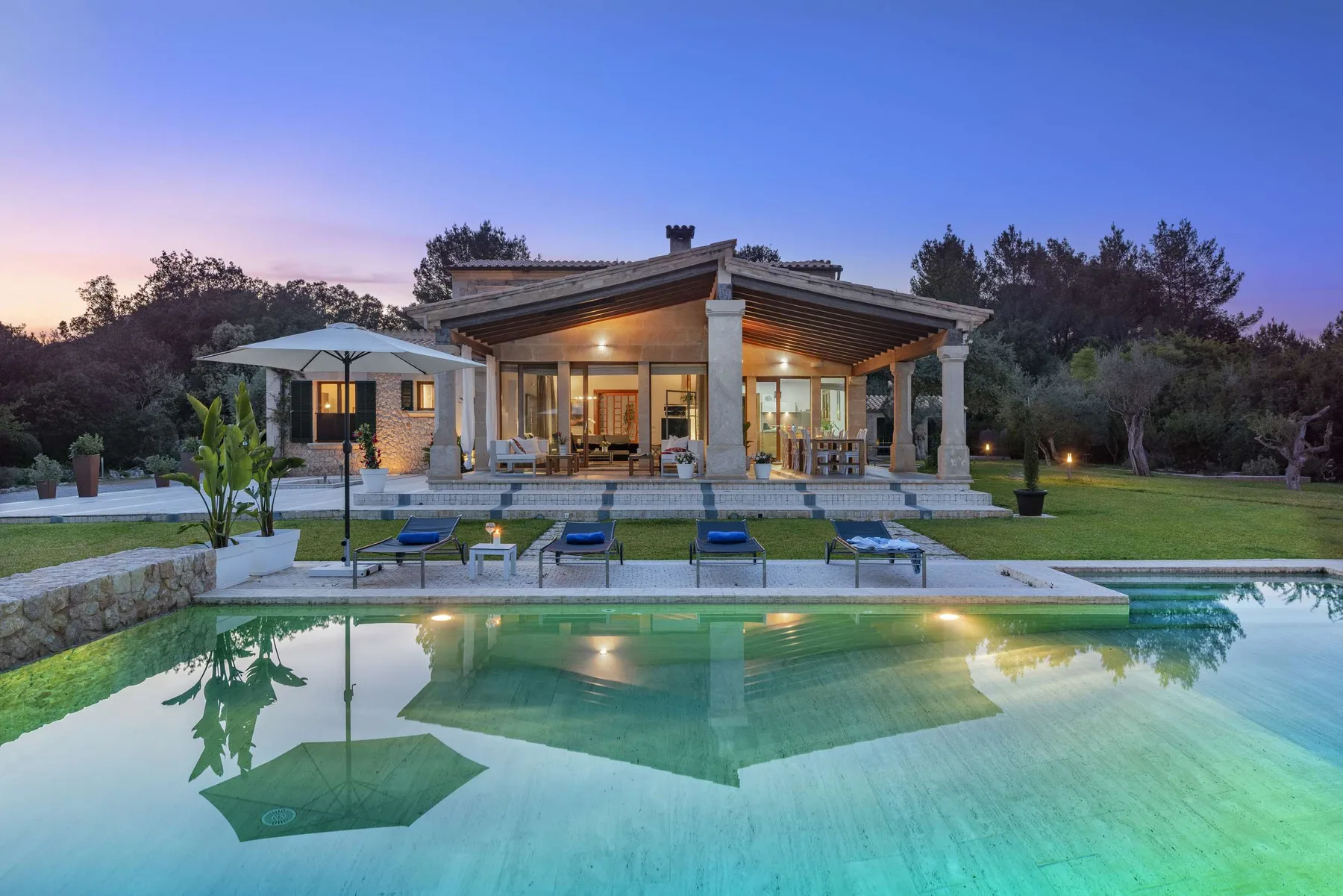 A modern house with a covered patio overlooks a swimming pool at dusk.