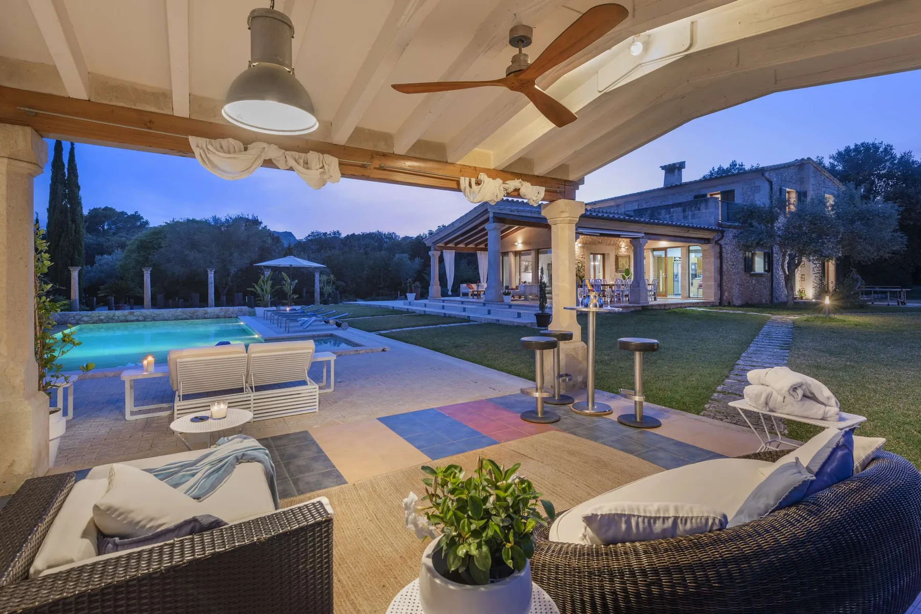 A covered patio with outdoor seating overlooks a swimming pool and landscaped grounds.