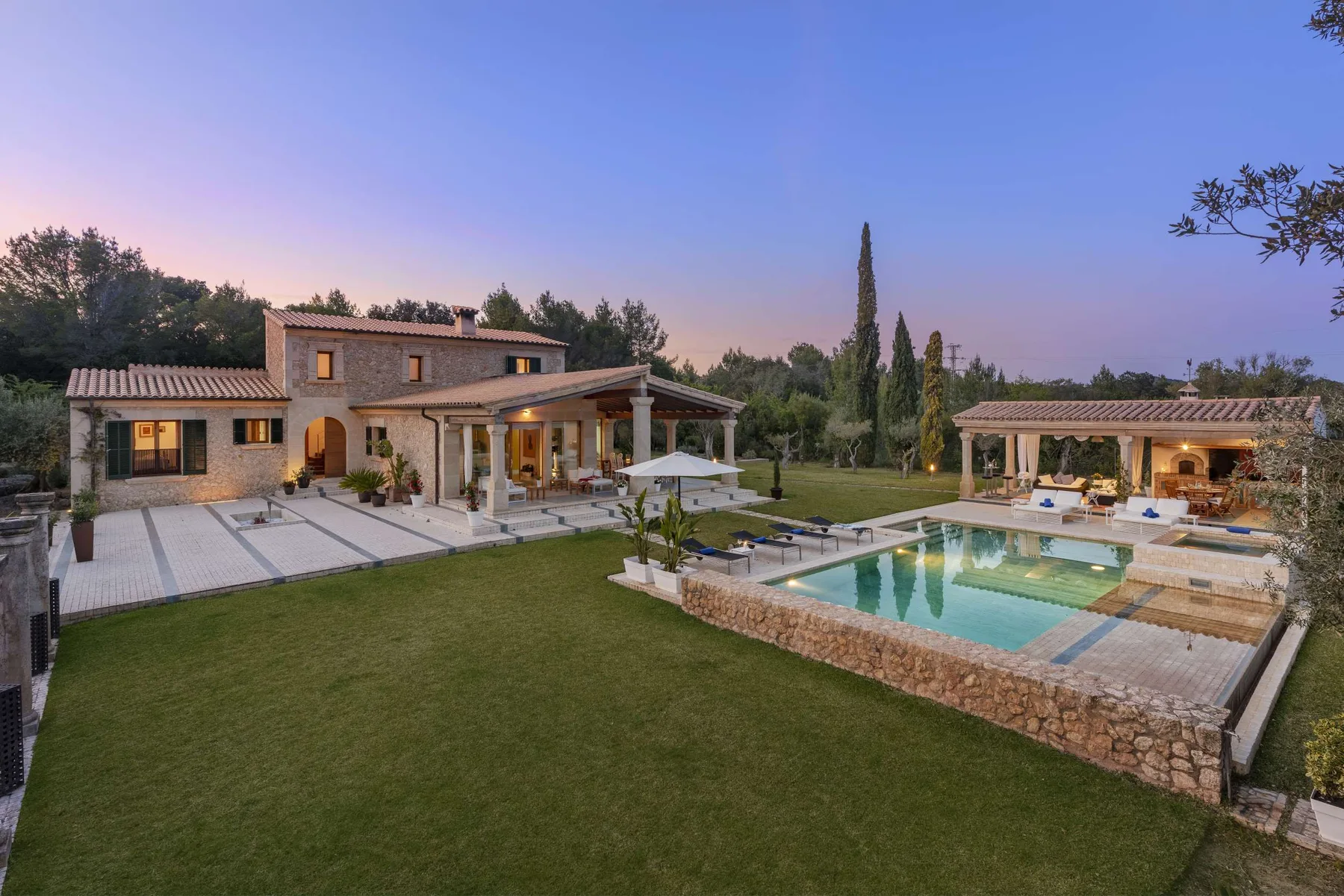 A landscaped outdoor pool beside a stone house and covered patio.