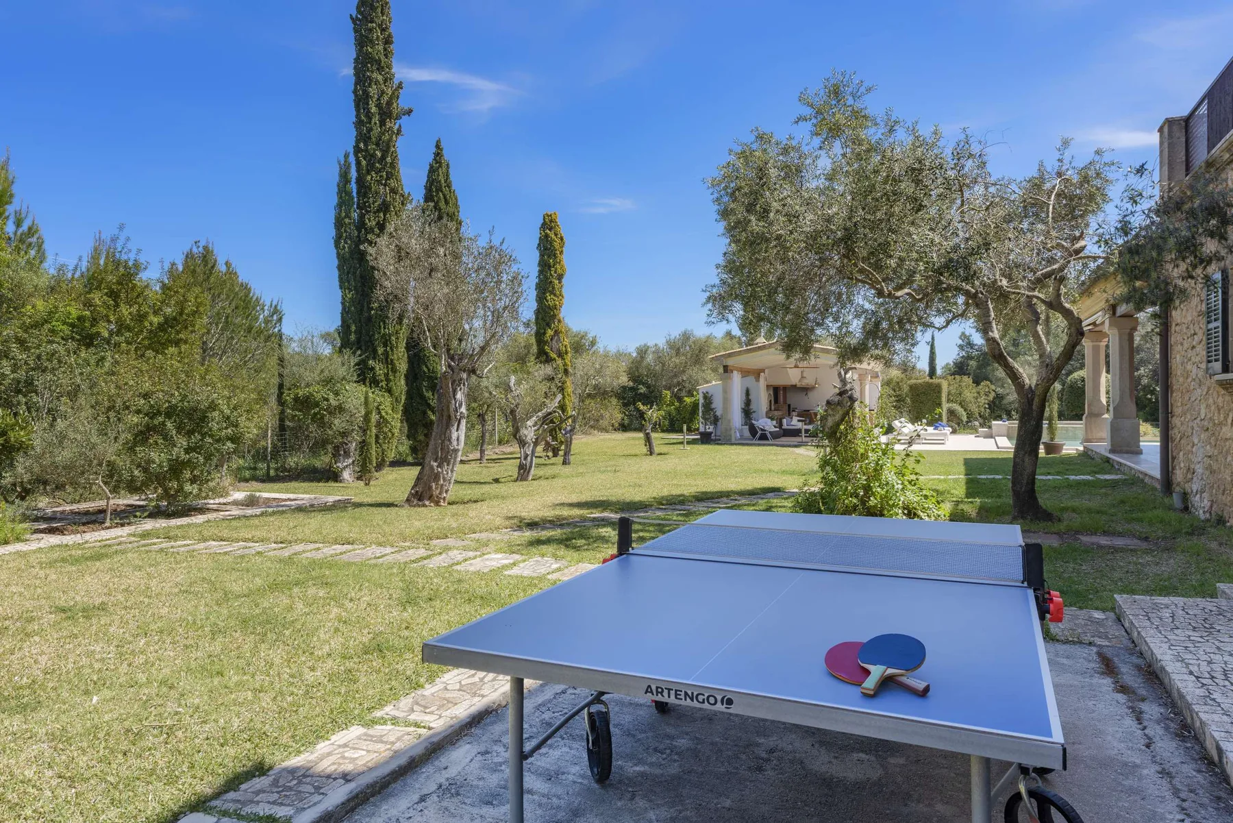 A garden with a table tennis table and trees beside a house.