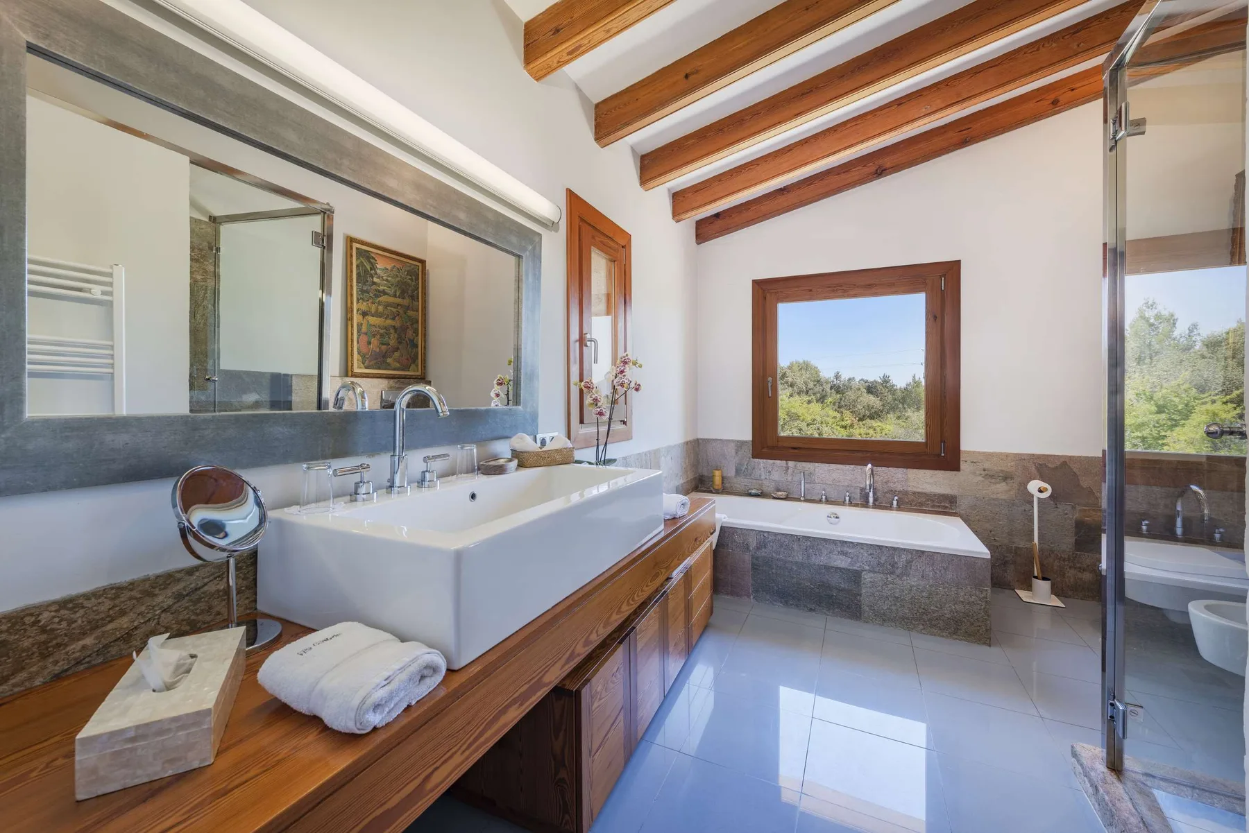 A bathroom with a large sink, bathtub, and window overlooking greenery.