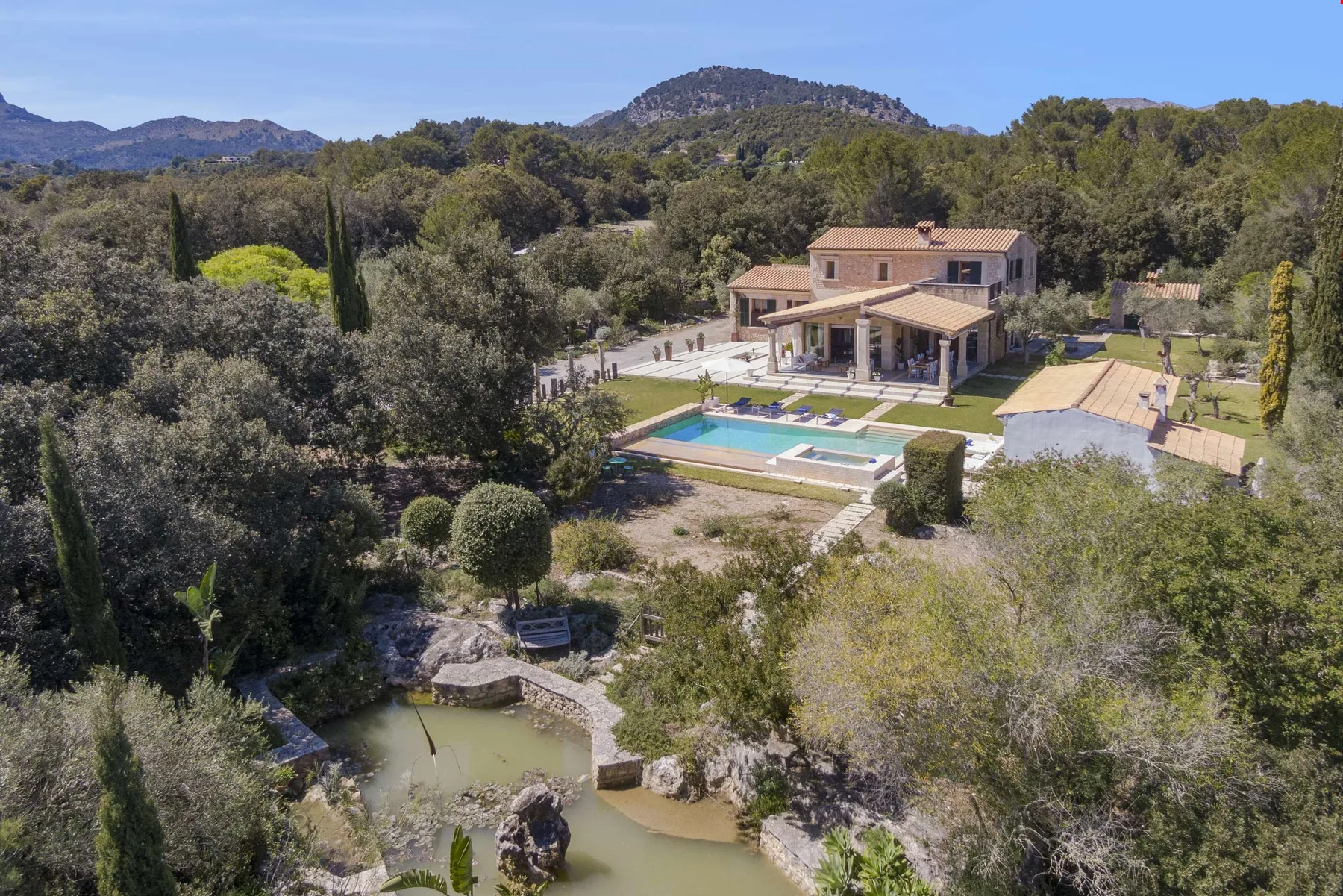 A countryside property overlooks a swimming pool and a small pond amid wooded hills.