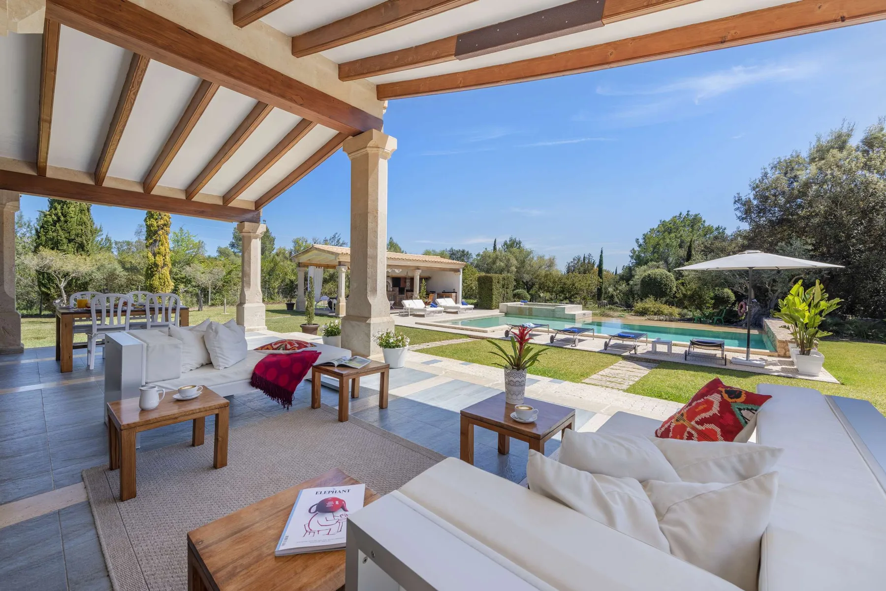 A covered outdoor seating area overlooks a swimming pool and landscaped garden.