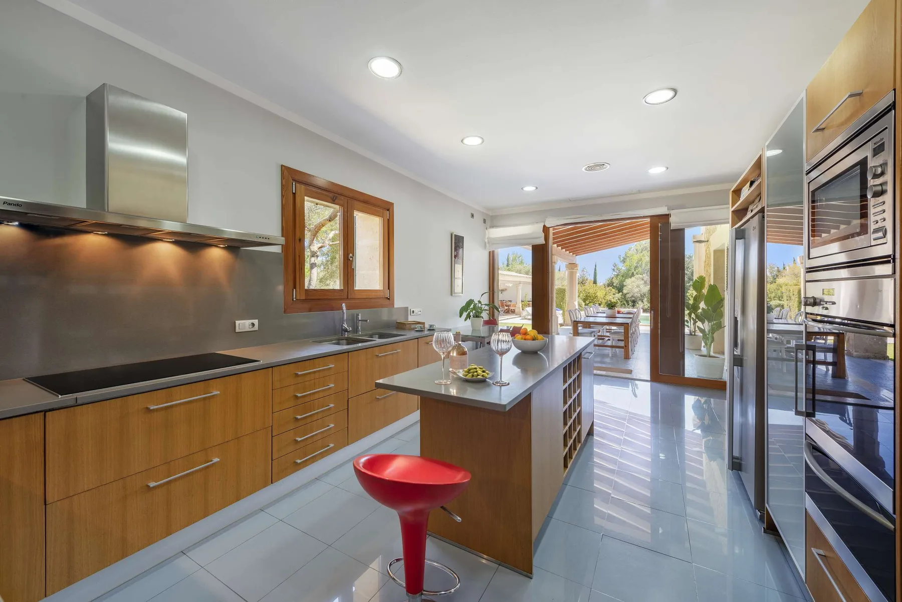 A modern kitchen with a central island opens onto an outdoor dining area.