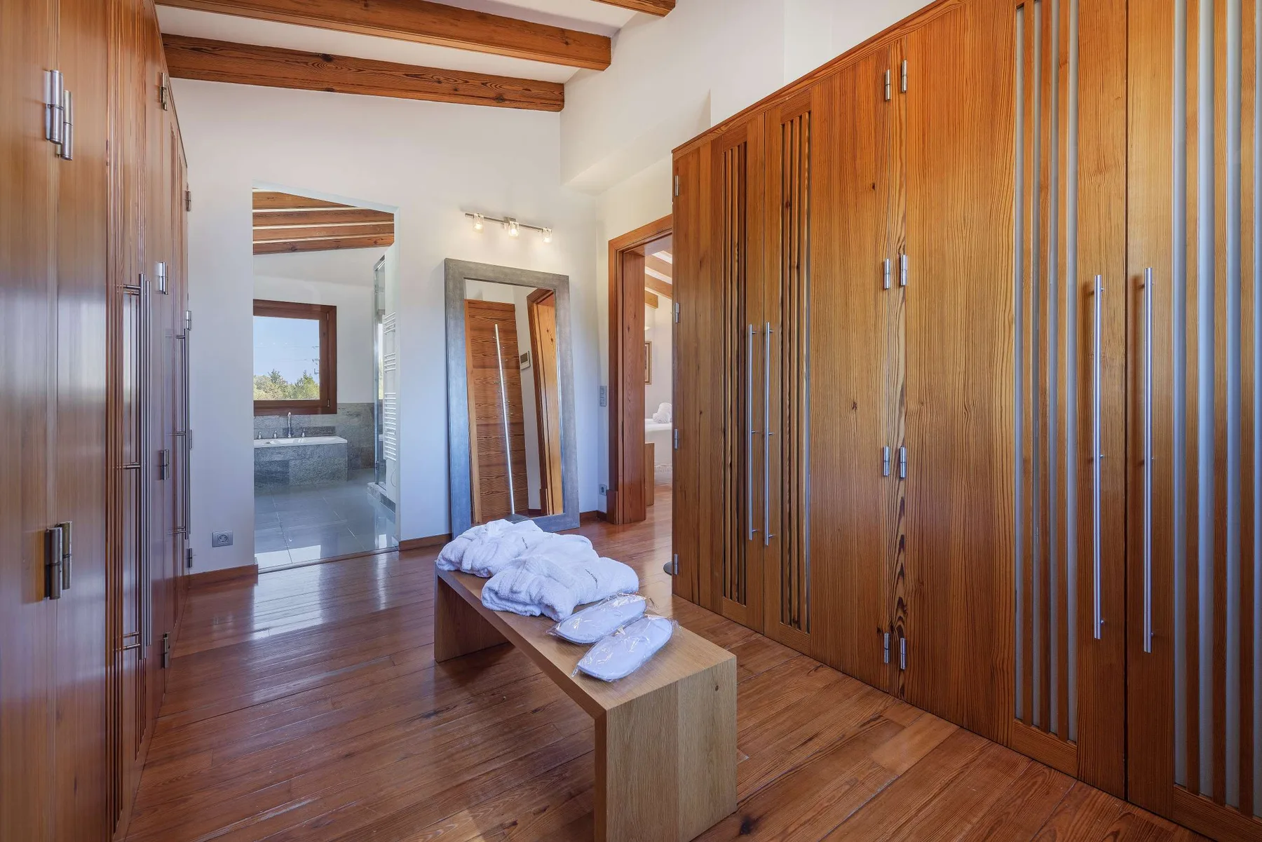 A bedroom dressing area with wooden wardrobes and folded linens on a bench.