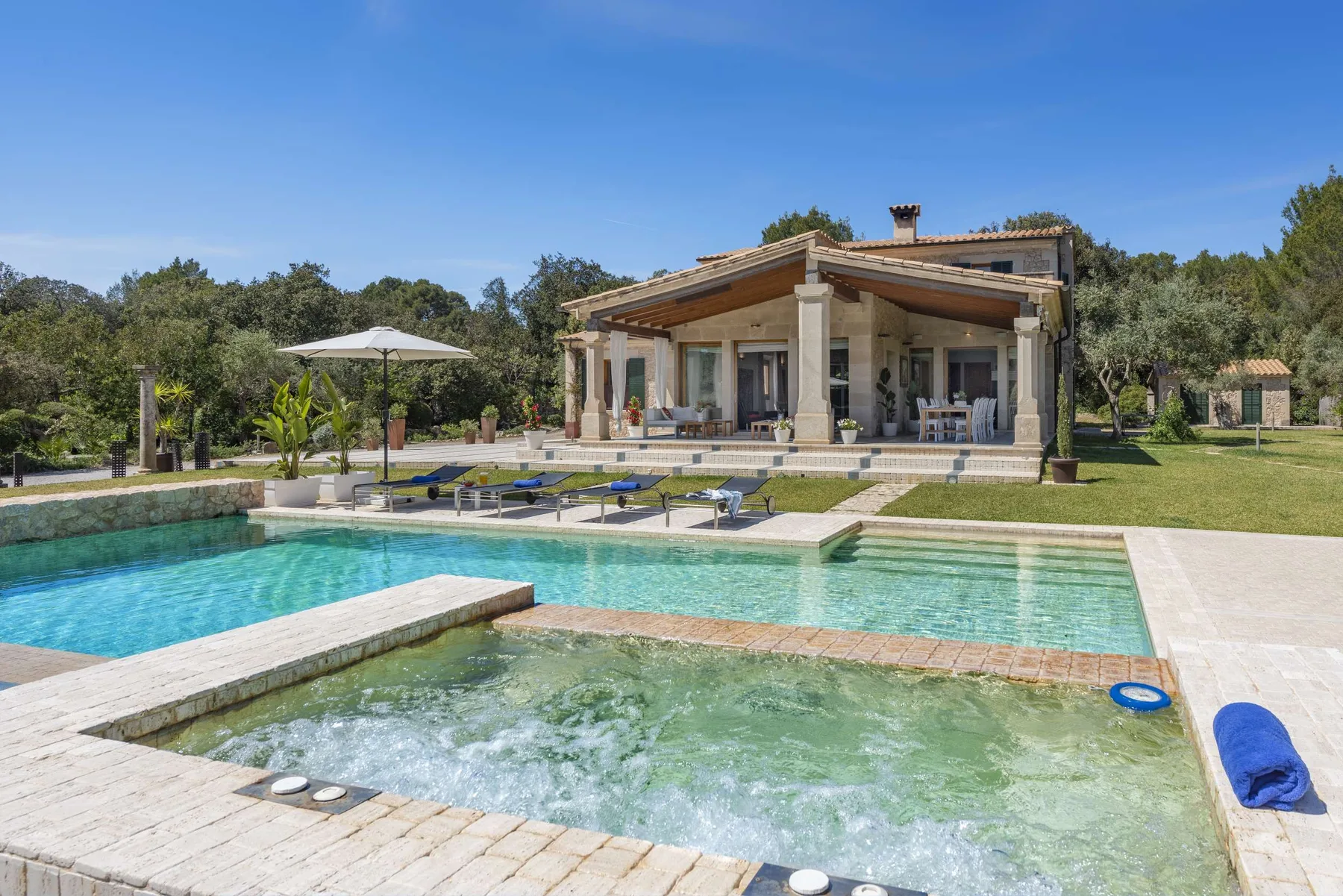A pool and bubbling spa sit in front of a house beneath a clear blue sky.