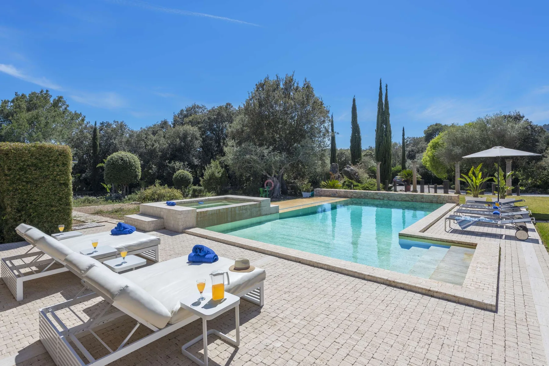An outdoor swimming pool is surrounded by paved decking, lounge seating, and greenery.