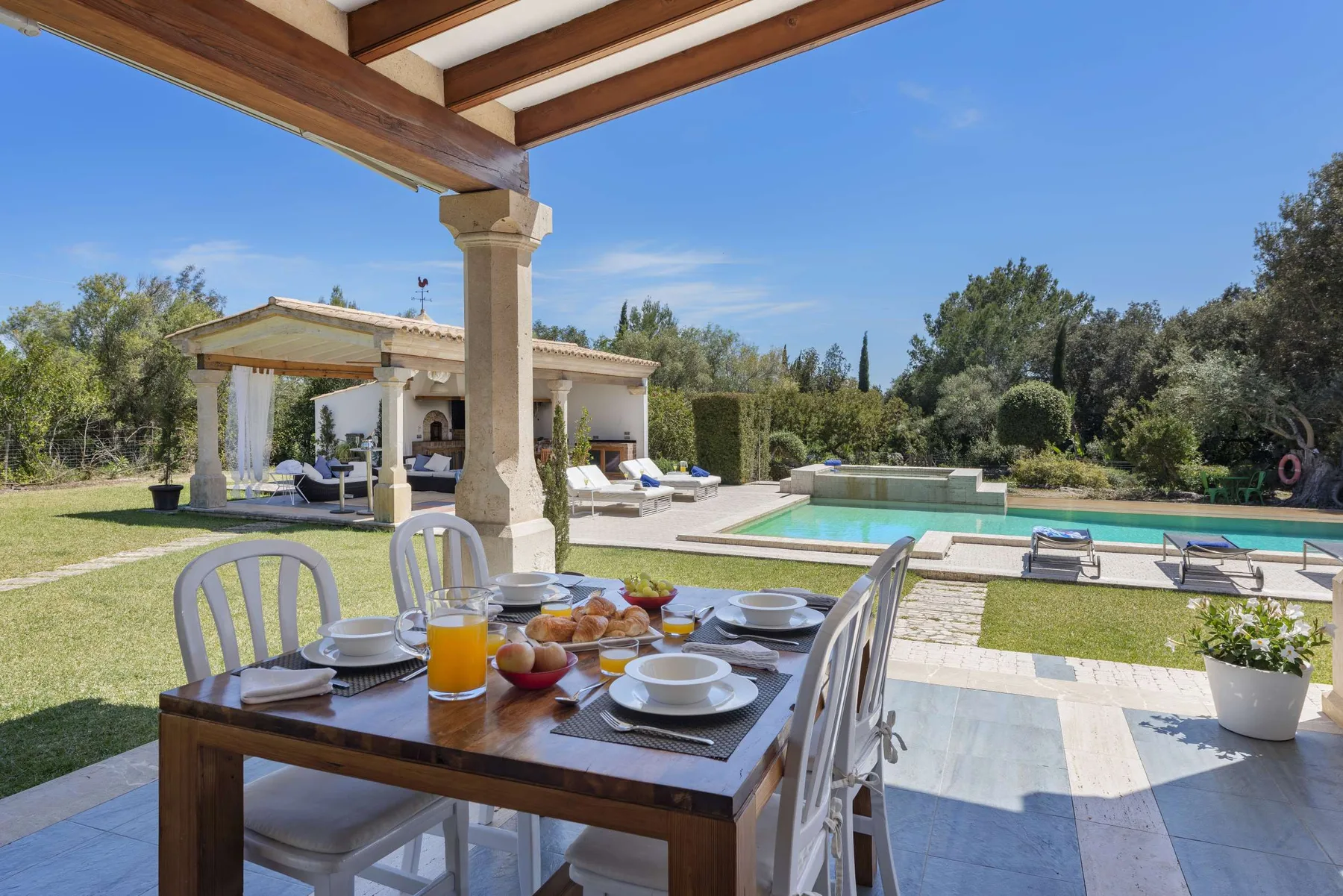 An outdoor dining area overlooks a swimming pool and landscaped garden.