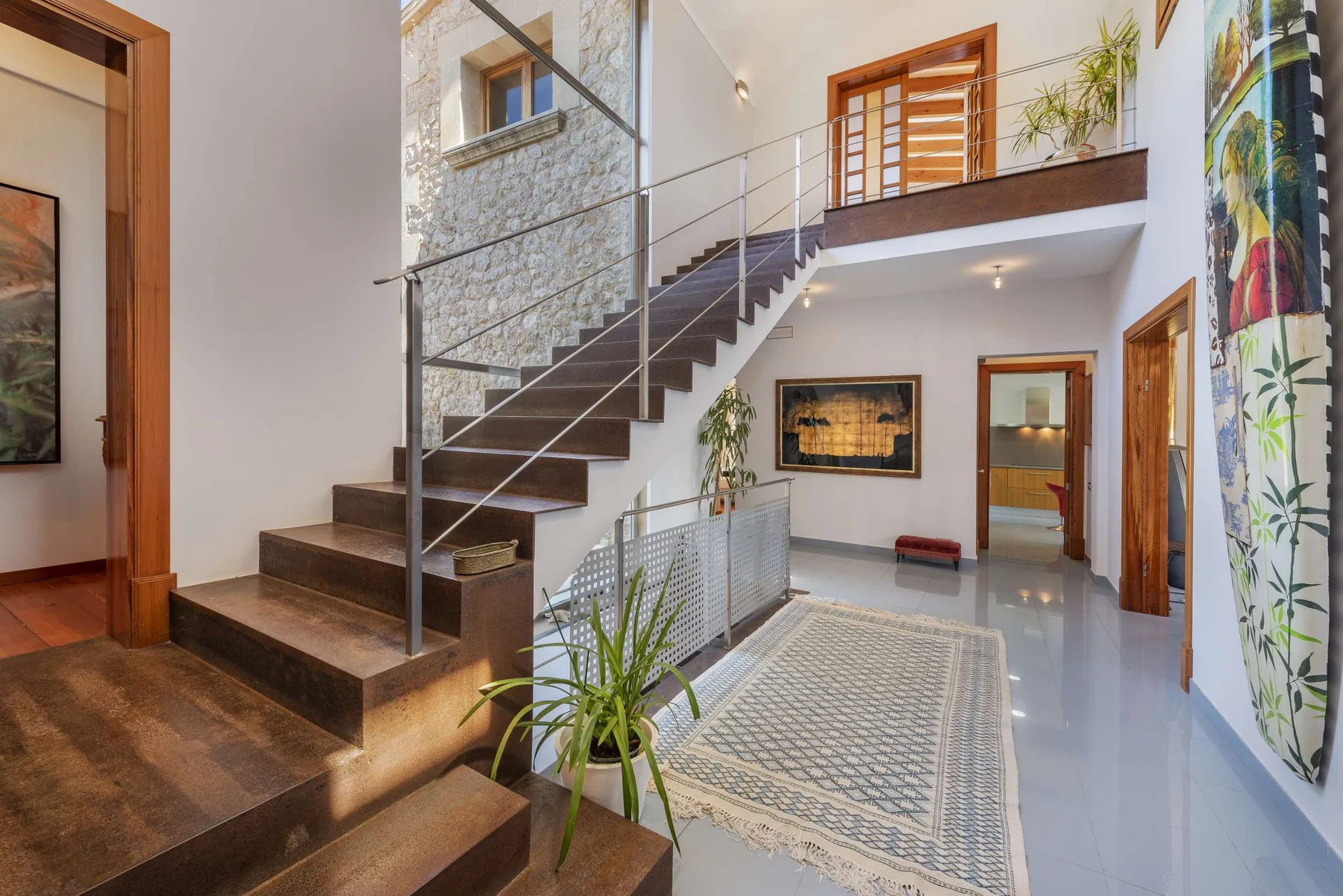 A bright interior hallway with a staircase, metal railing, and patterned rug.