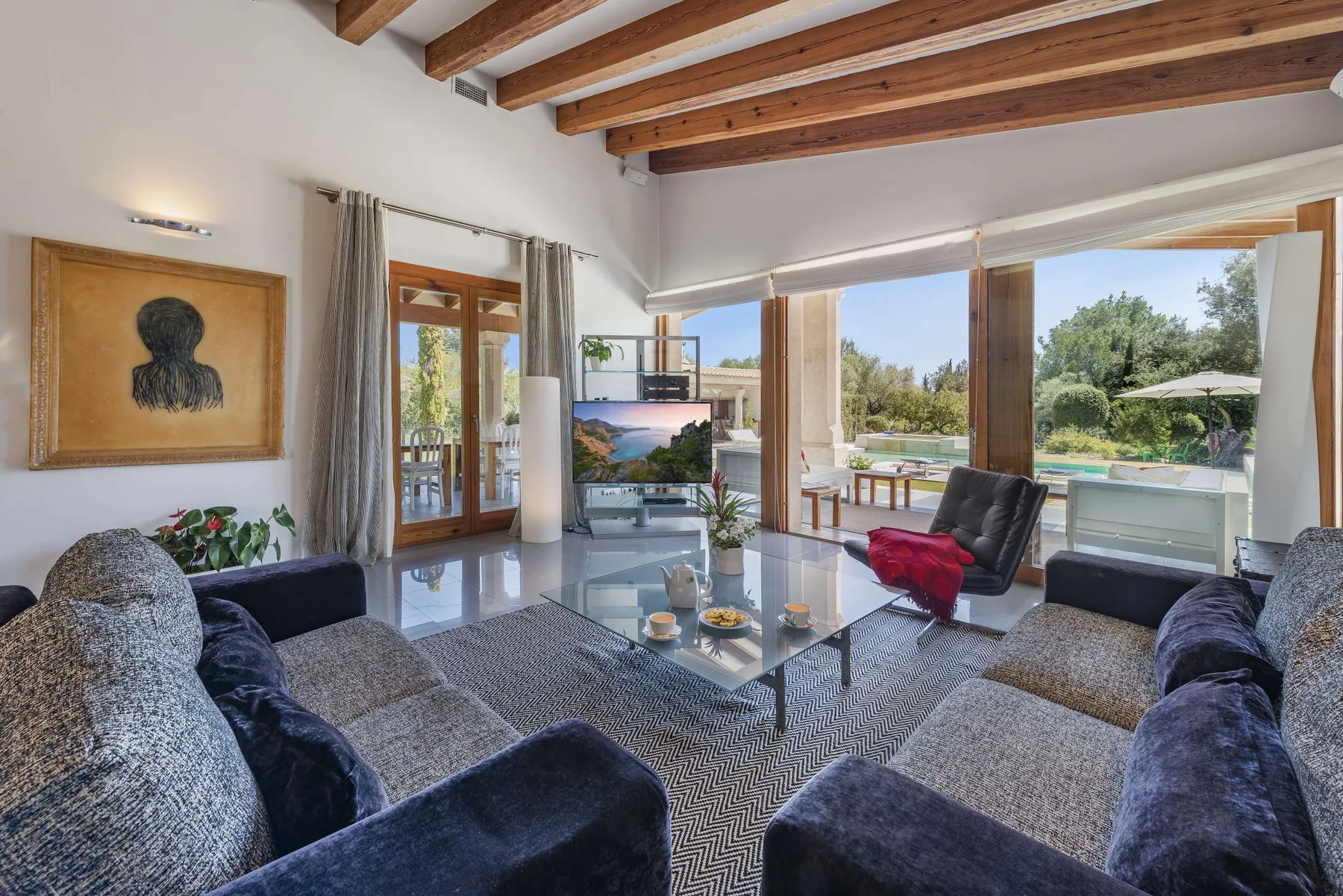 A bright living room with seating, a glass coffee table, and large windows.