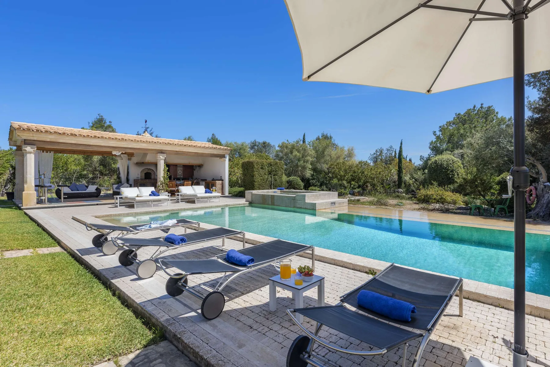 A swimming pool and sun loungers sit beside a shaded outdoor seating area.