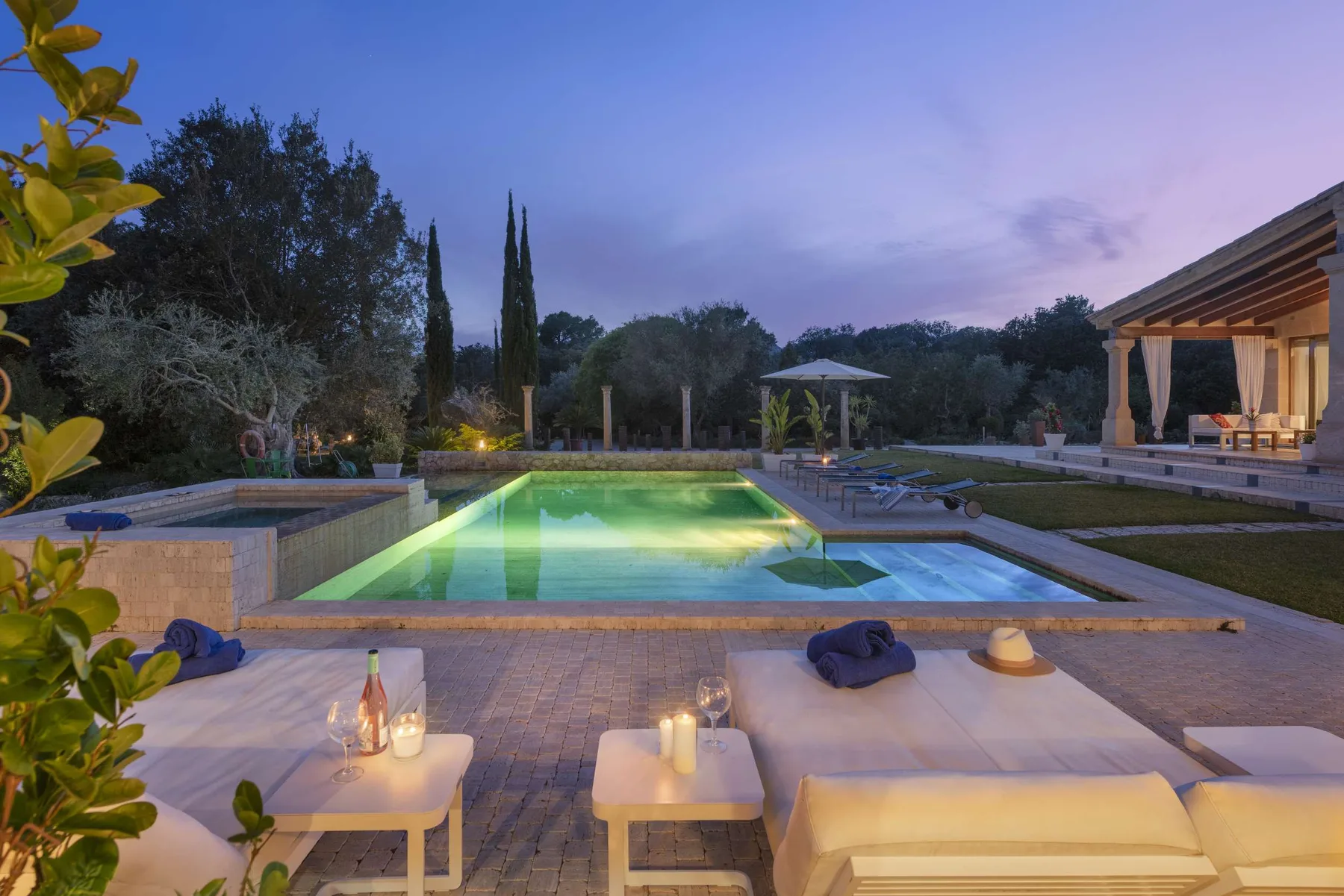 An outdoor pool beside a patio seating area at dusk.