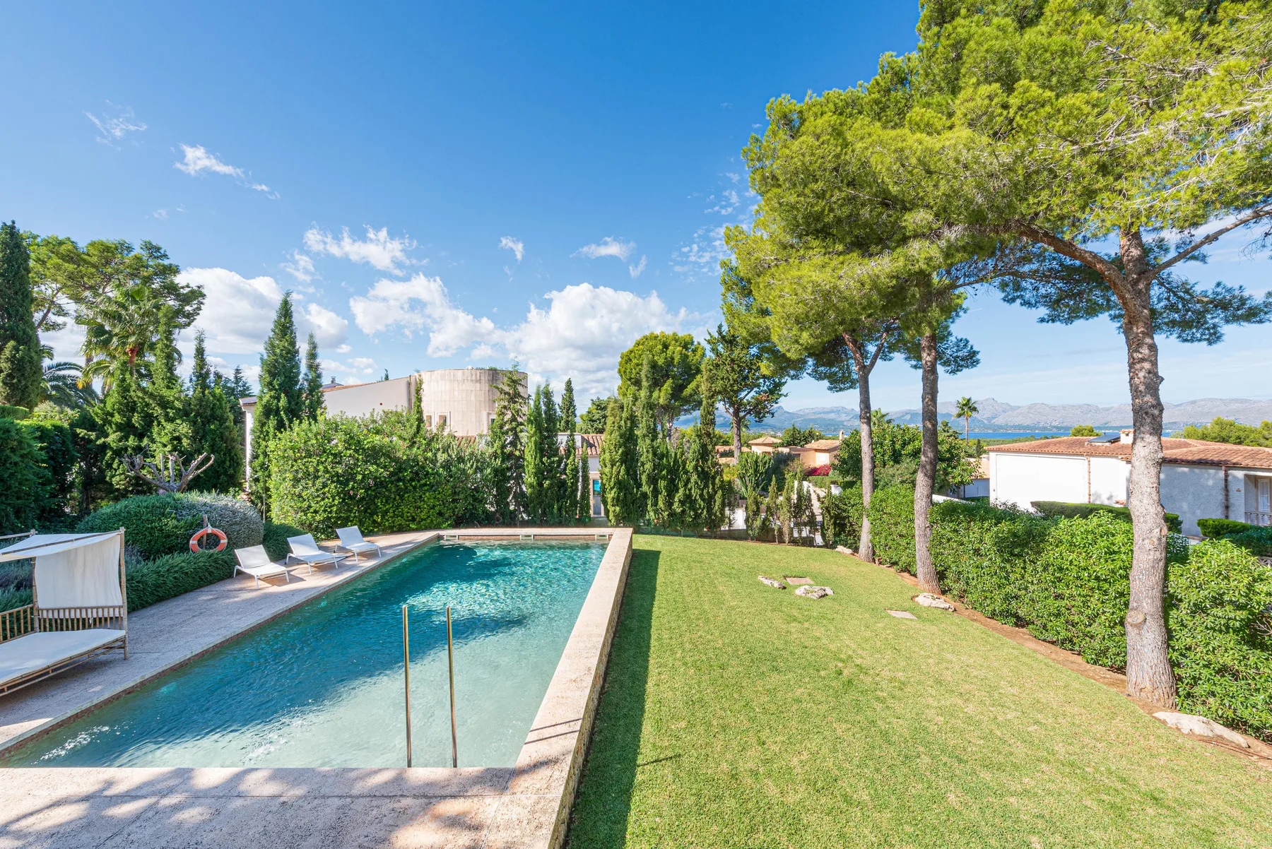 An outdoor pool beside a grassy lawn, tall trees, and garden hedges.