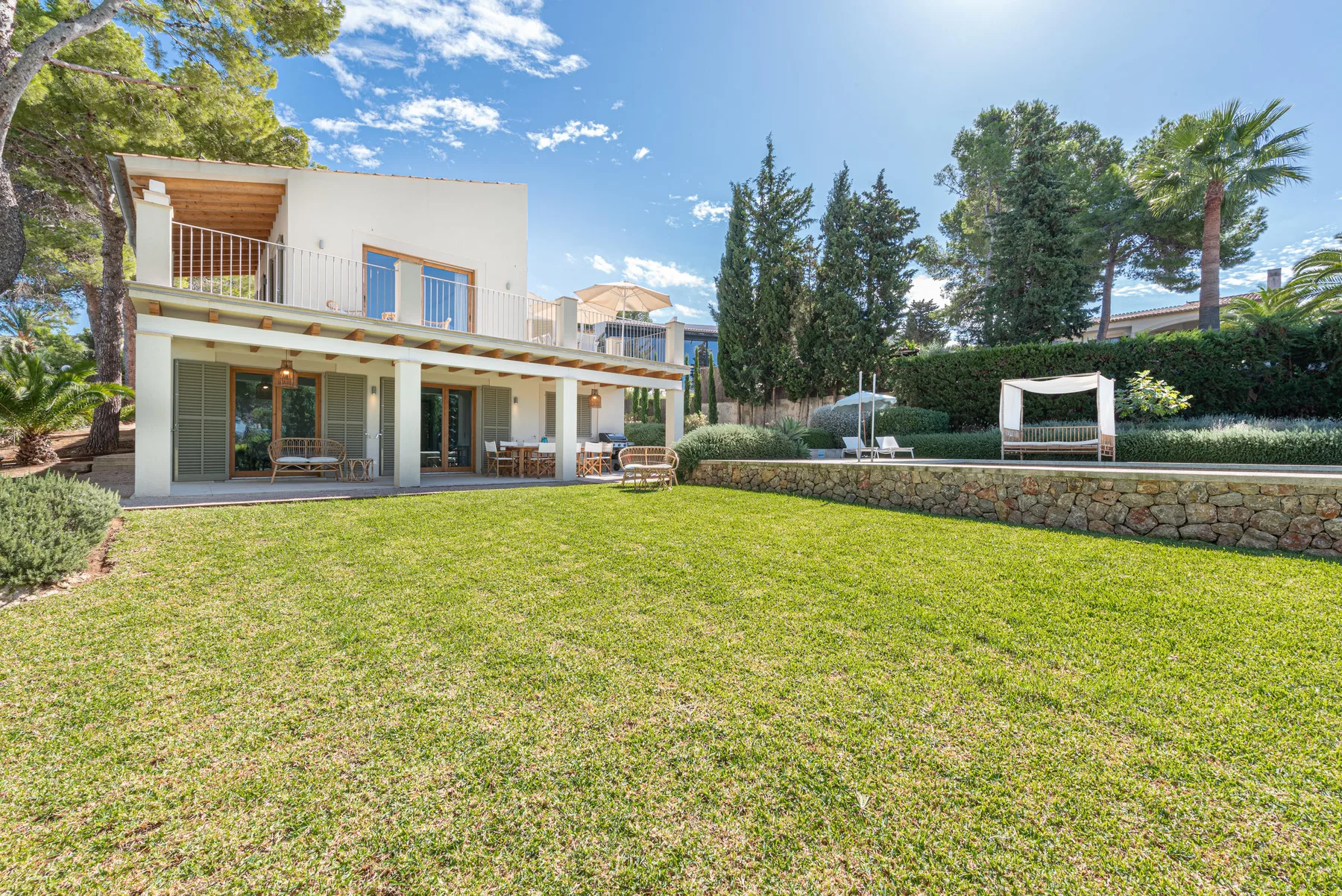 A modern house opens onto a broad lawn, with trees and a garden seating area.