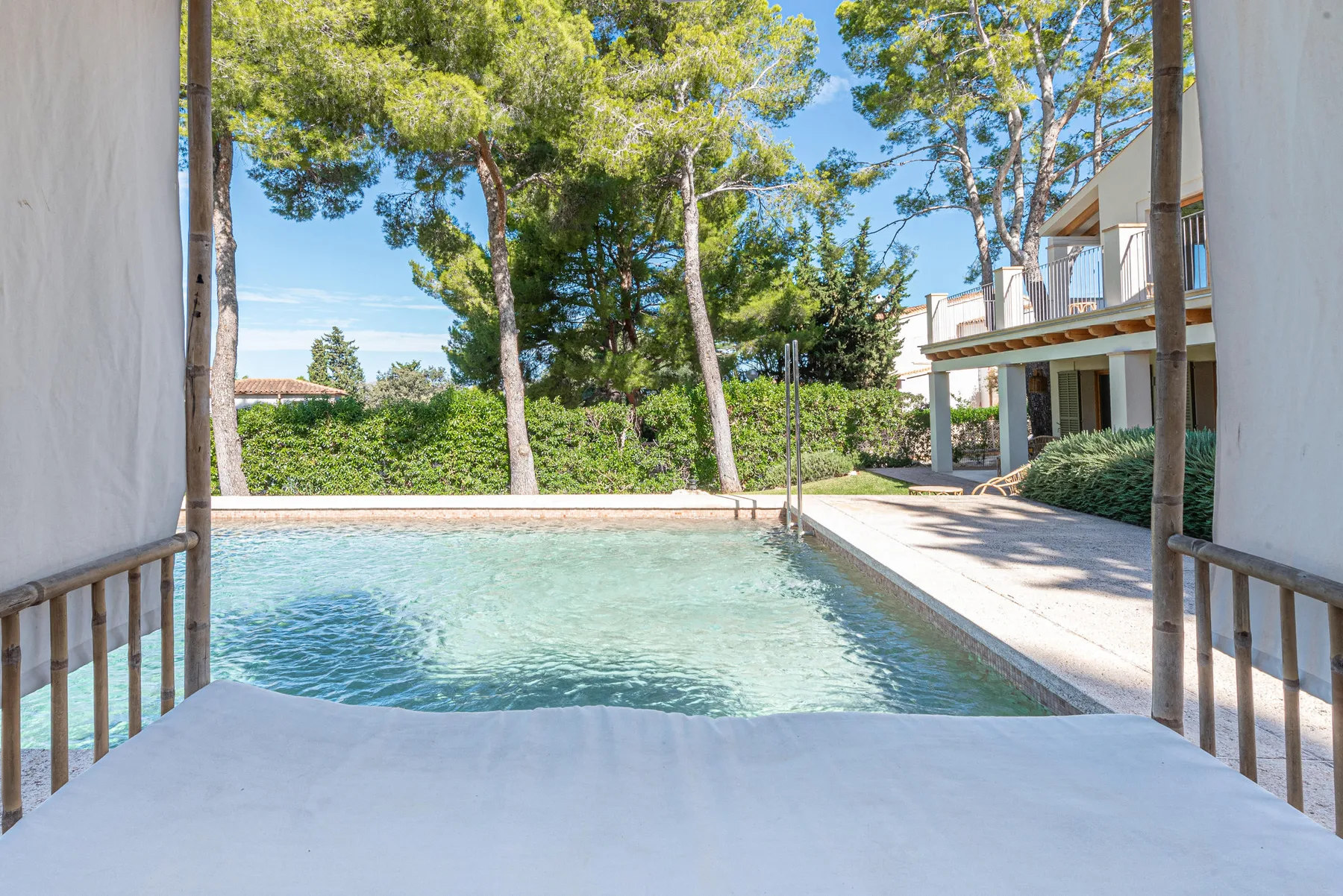 A swimming pool sits beside a paved patio, with trees and a building in the background.