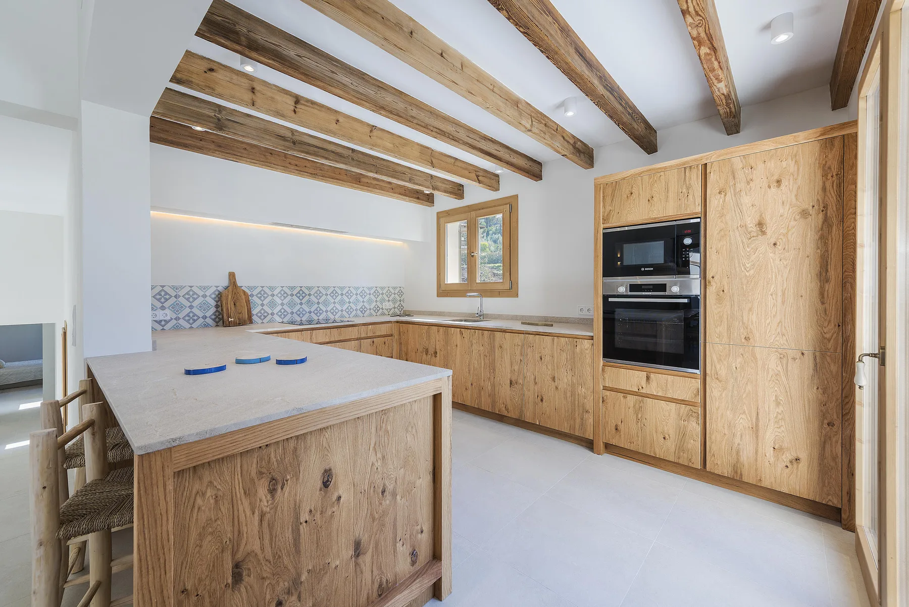 A bright kitchen with wood cabinetry, exposed ceiling beams, and a central island.