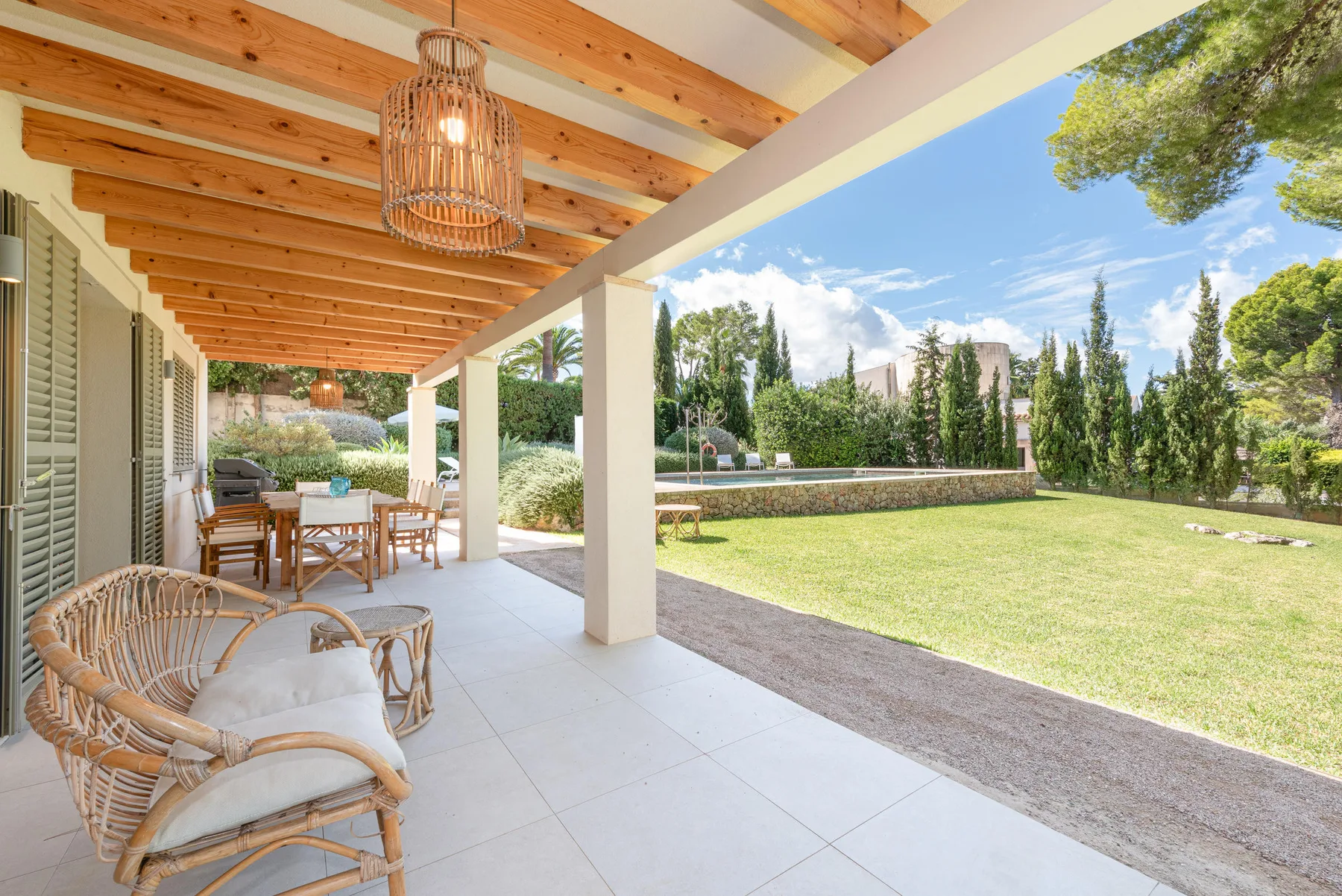 A covered patio with seating overlooks a lawn and garden.