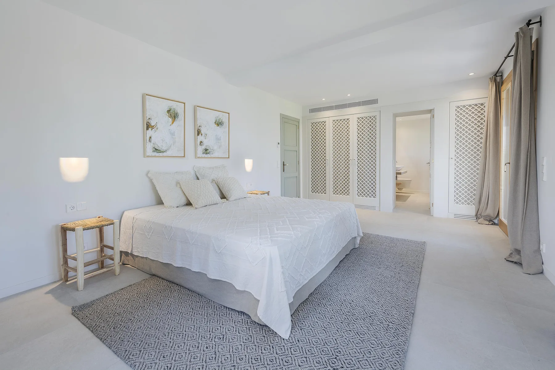 A bright bedroom with a neatly made bed and a large patterned rug.