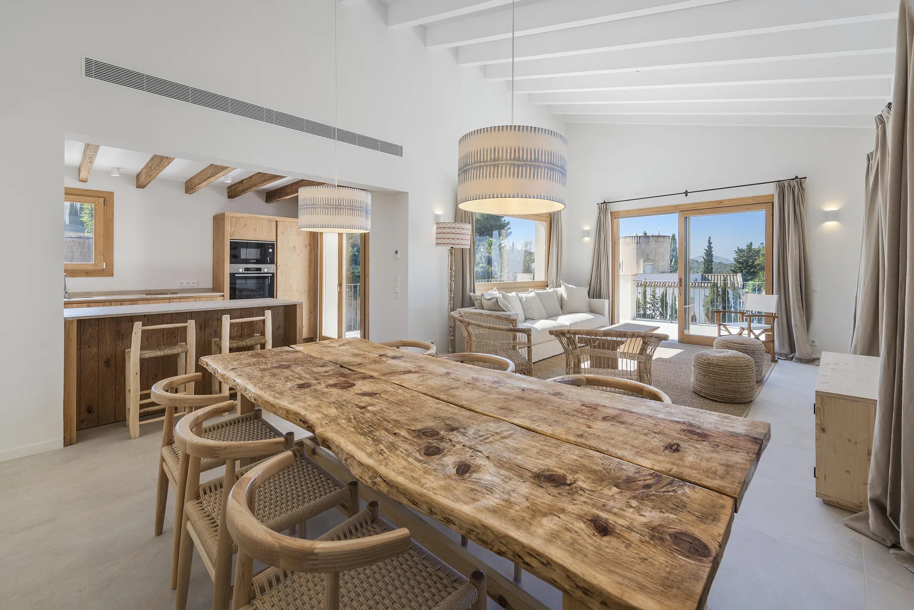 A bright open-plan dining and living area with a long wooden table and seating.
