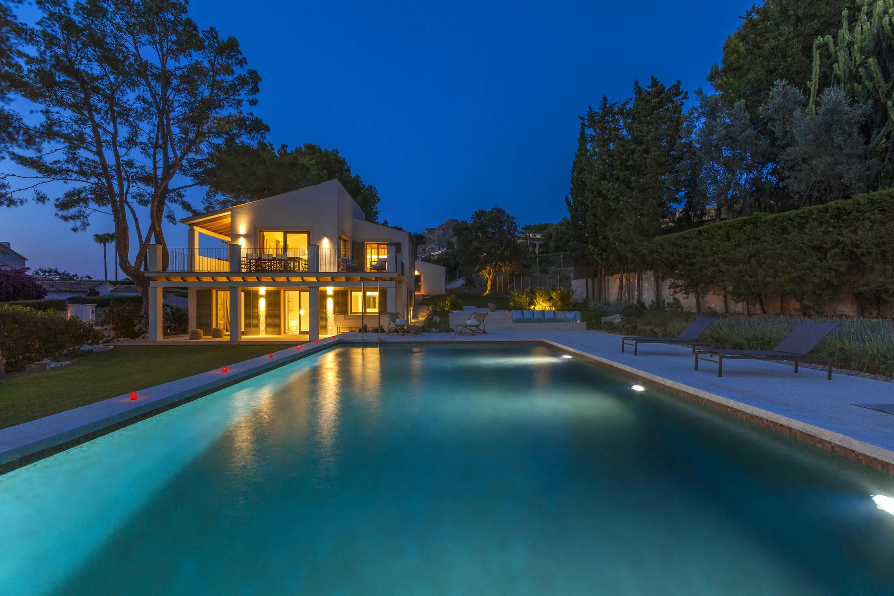 A swimming pool at dusk overlooks a modern house with illuminated windows.