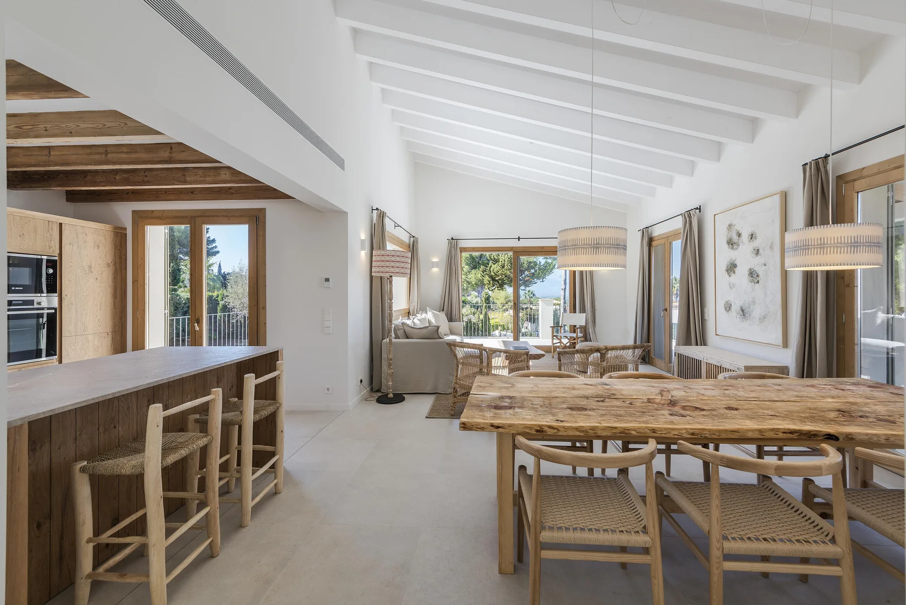 A bright open-plan dining and living area with a large wooden table and kitchen counter.