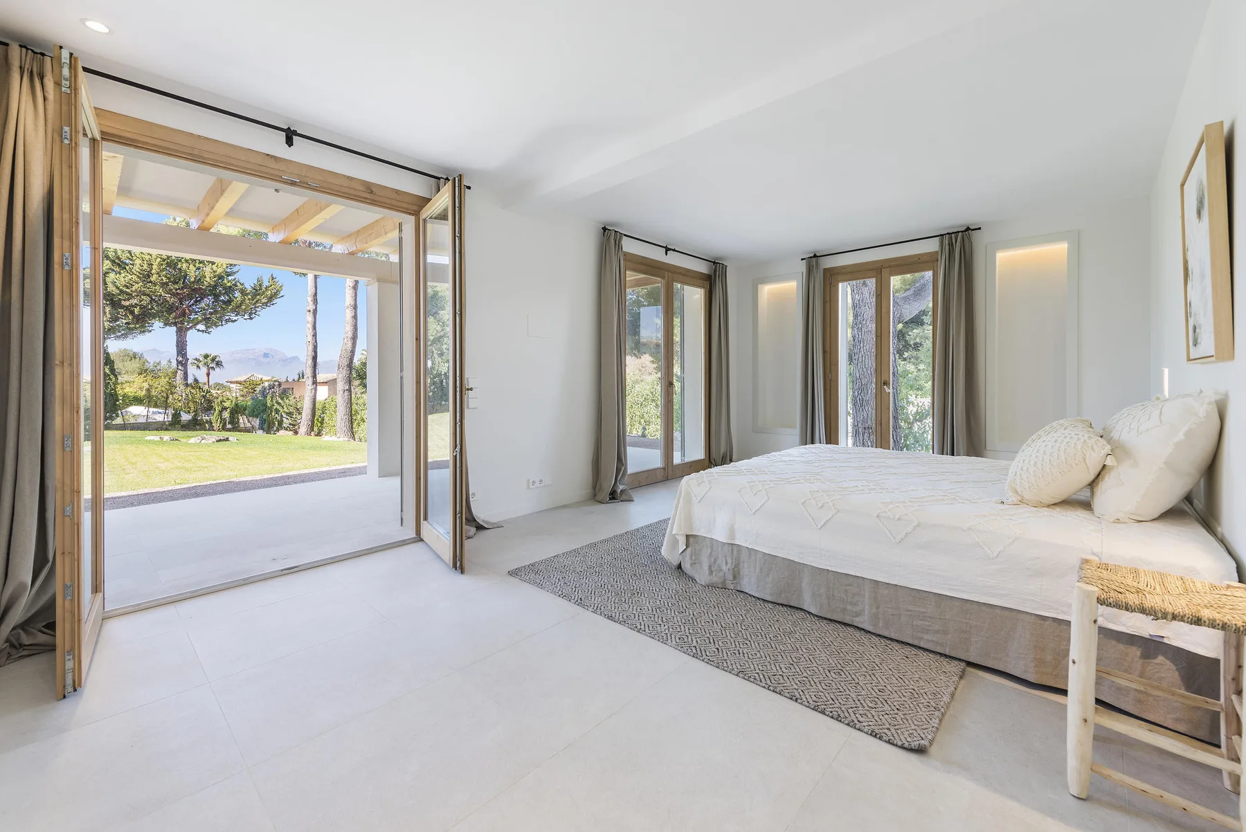 A bright bedroom with a bed and open doors leading to a garden.