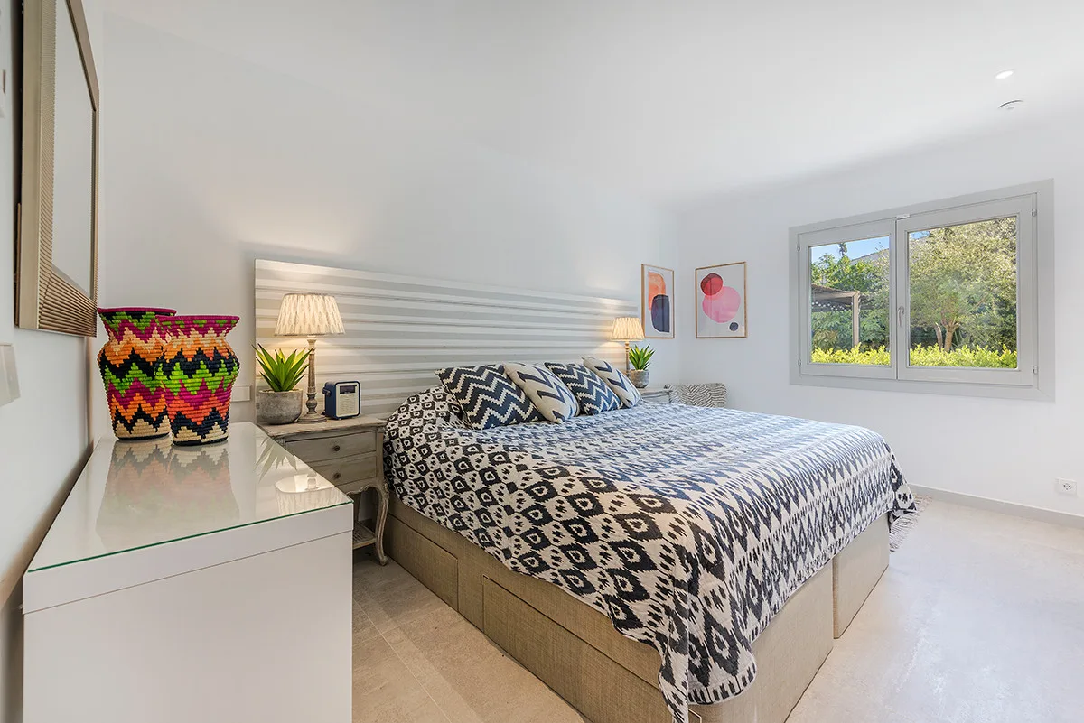 A bright bedroom with a large bed and a window overlooking greenery.