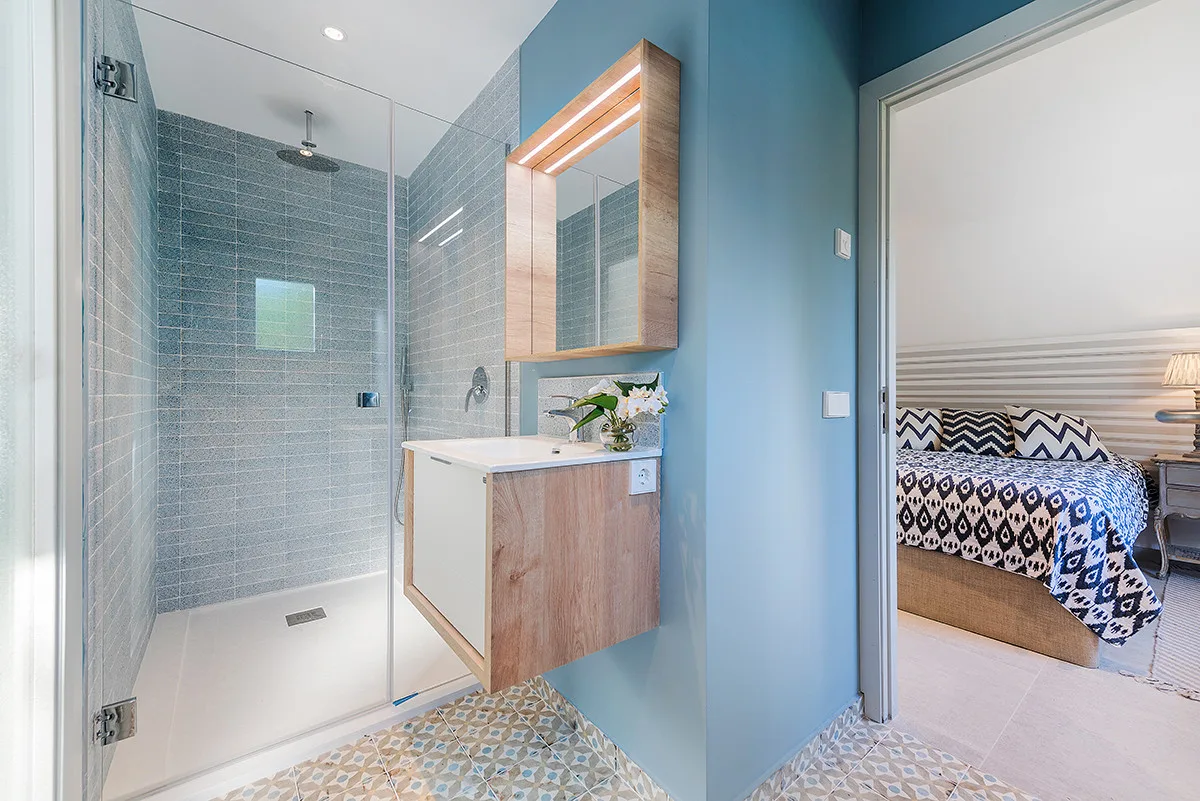A bathroom with a glass shower and vanity beside an open doorway to a bedroom.