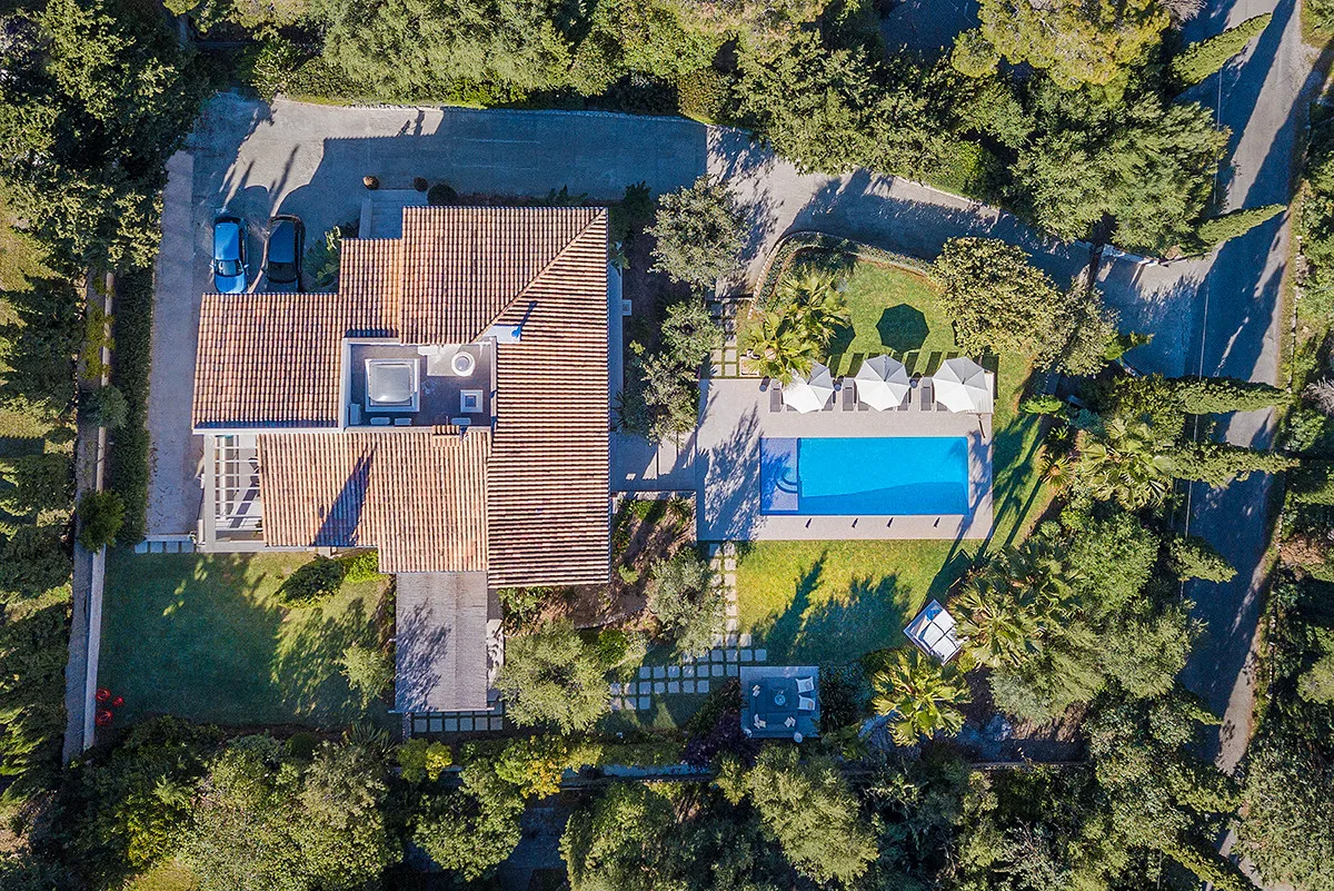 An aerial view shows a house beside a rectangular swimming pool, surrounded by trees.