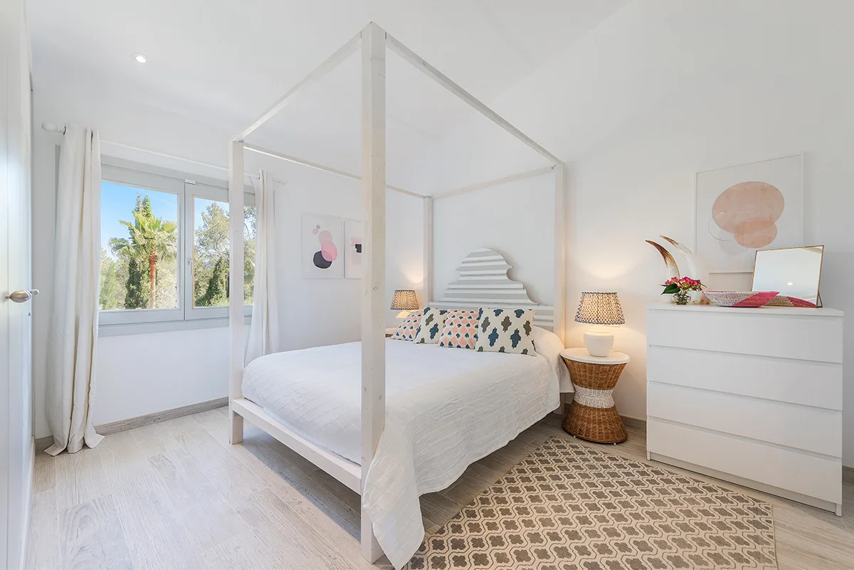 A bright bedroom with a canopy bed, bedside lamps, and a patterned rug.