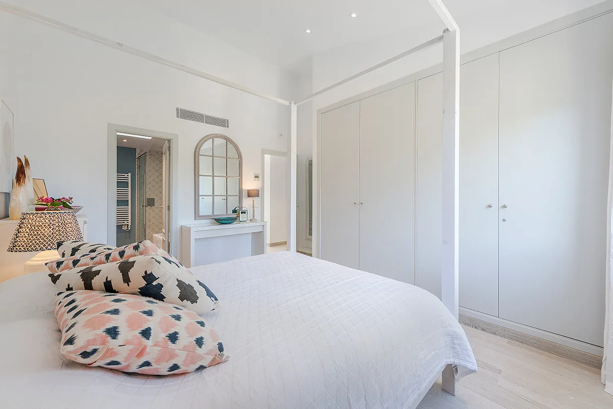 A bright bedroom with a white bed and built-in wardrobes.