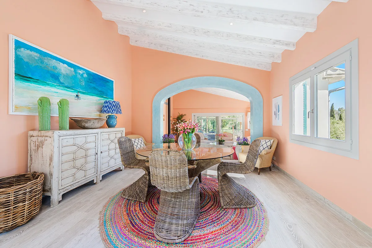 A dining area with woven seating around a table on a colorful circular rug.