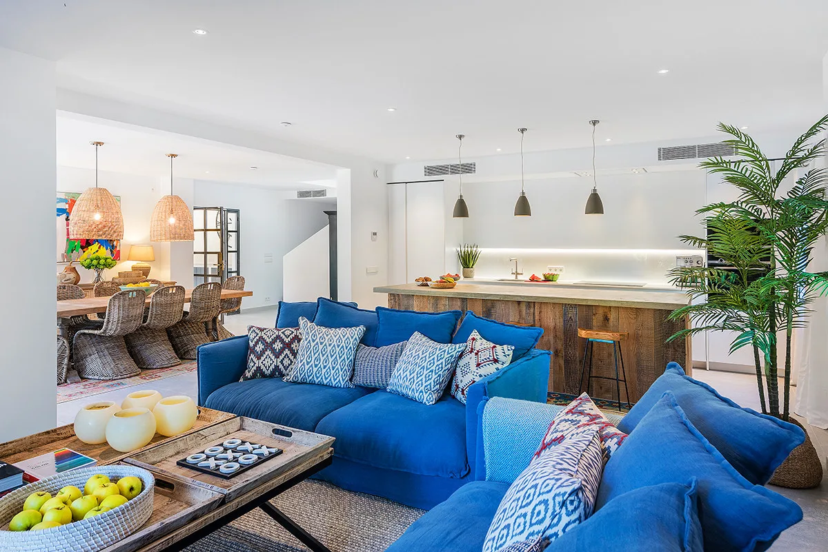 A bright open-plan living room with blue seating and a kitchen island.