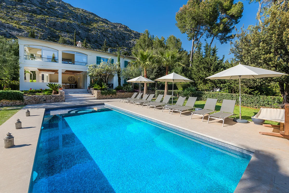 An outdoor swimming pool sits beside a modern building, with loungers and umbrellas along the deck.