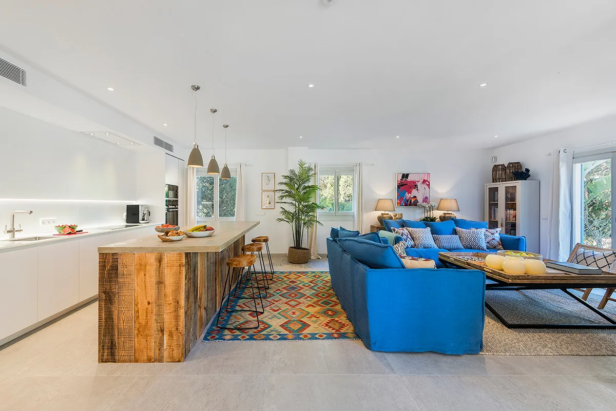 A bright open-plan living room and kitchen with blue seating around a low table.