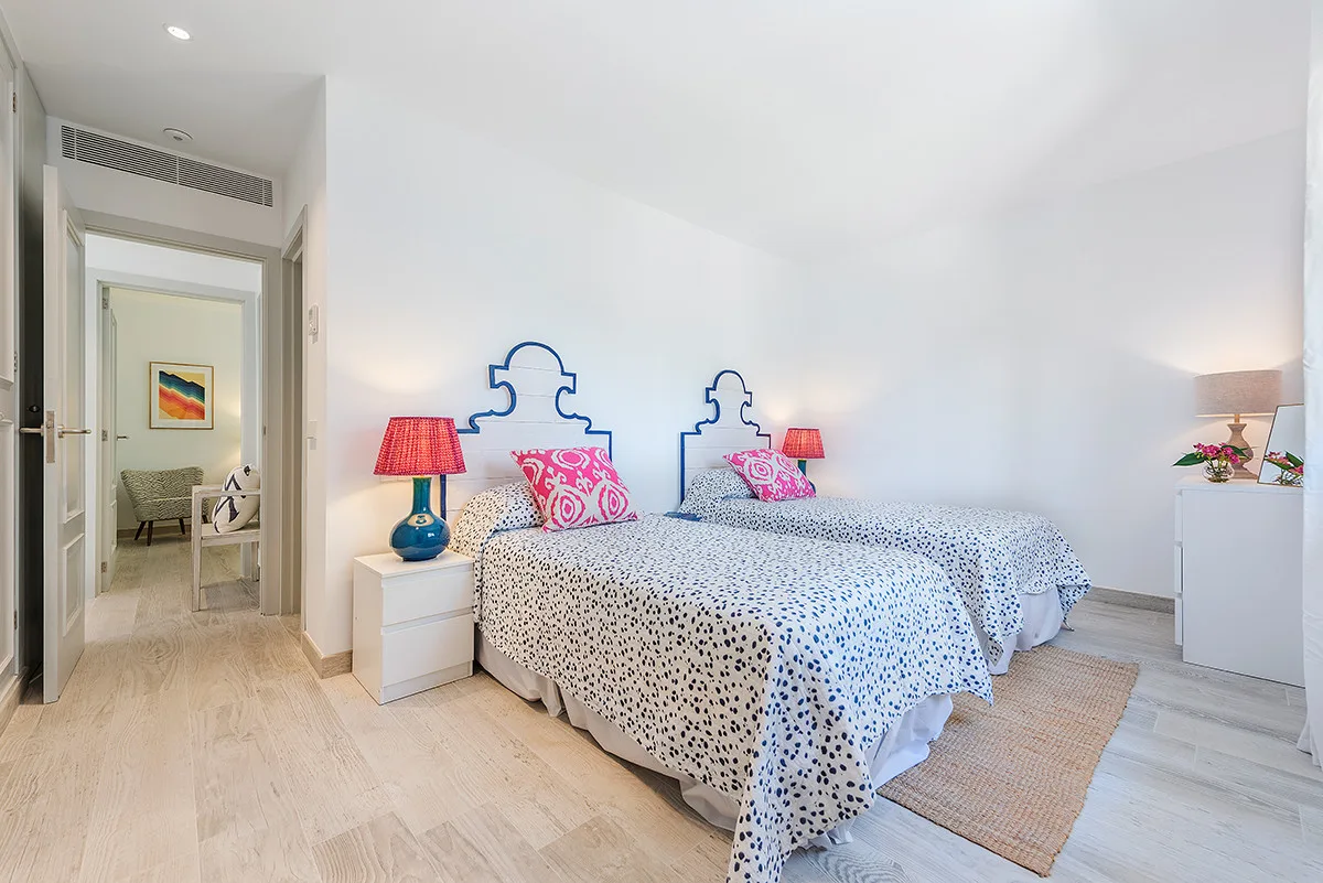 A bright bedroom with two beds and colorful bedside lamps.