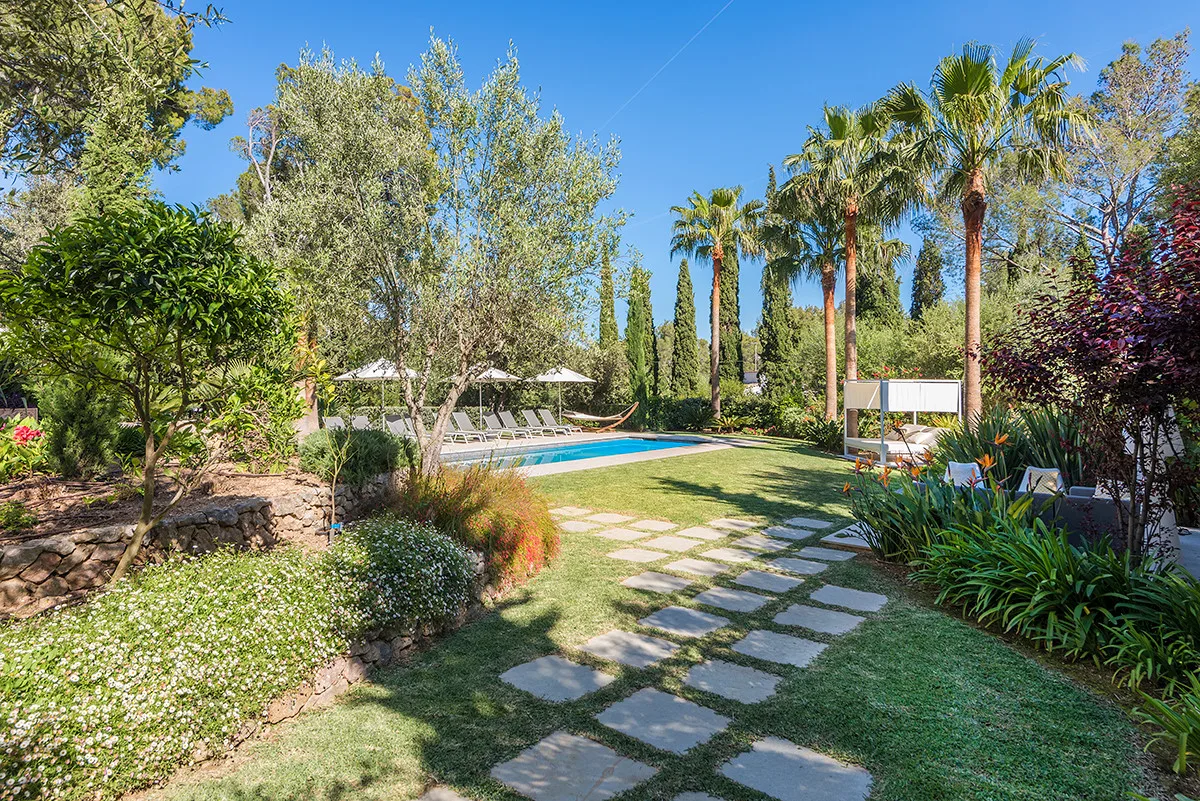 A garden path leads toward a swimming pool surrounded by trees and greenery.