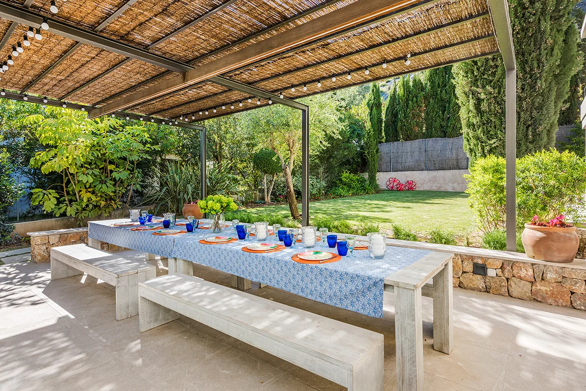 A covered outdoor dining area has a long table set with colorful plates and glasses.
