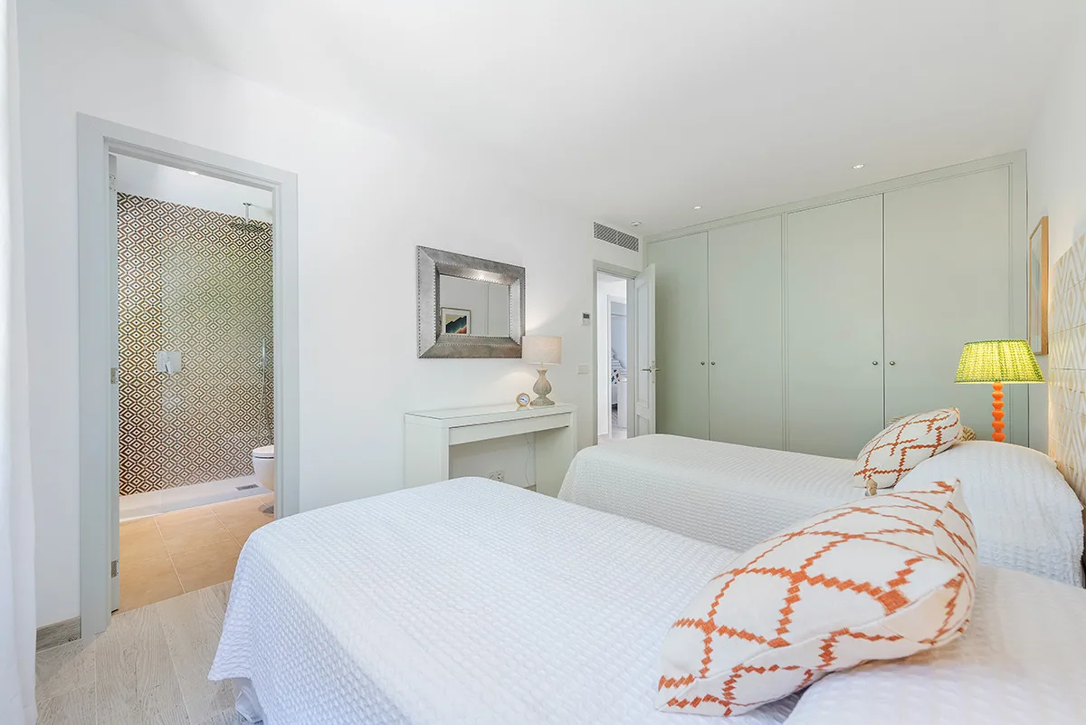 A bright bedroom with white bedding, patterned pillows, and built-in wardrobes.