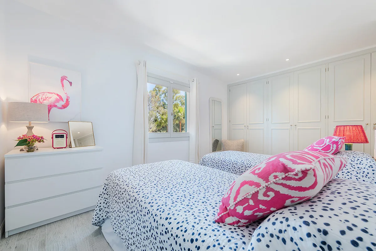 A bright bedroom with patterned bedding and built-in wall cabinets.