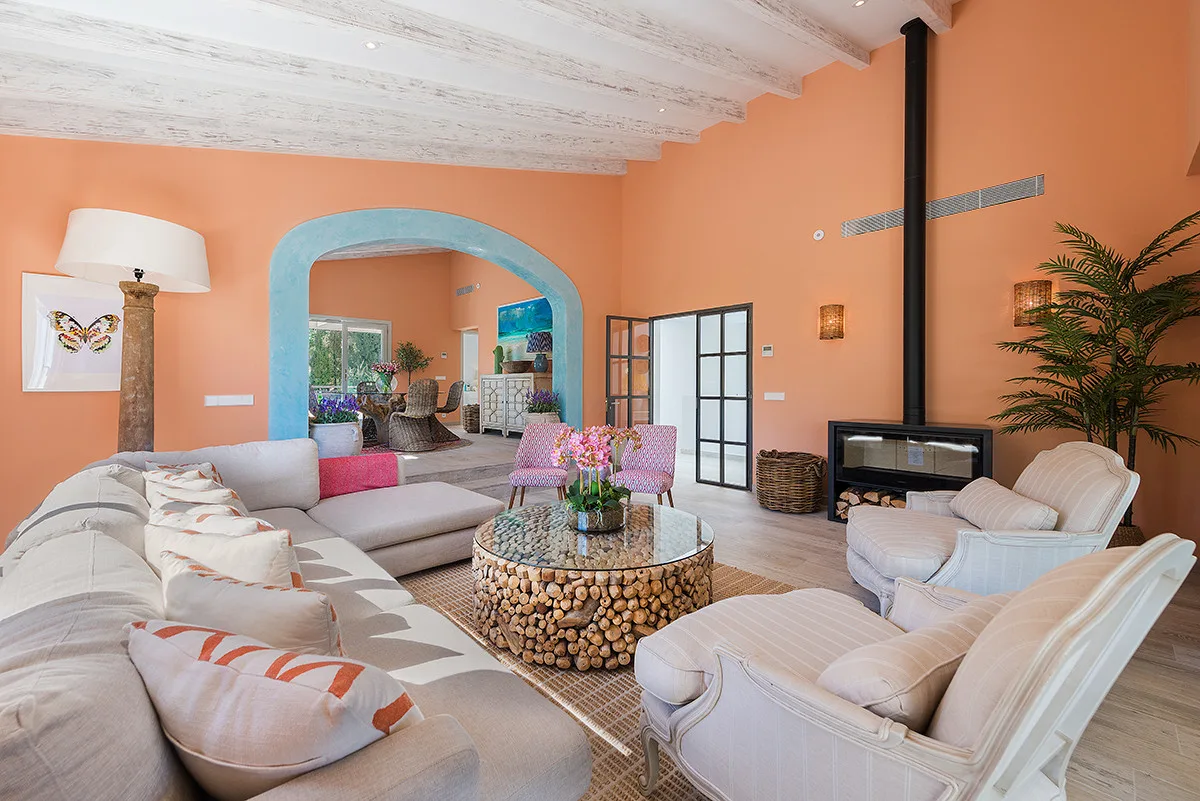 A bright living room with pale seating, a round coffee table, and a fireplace.